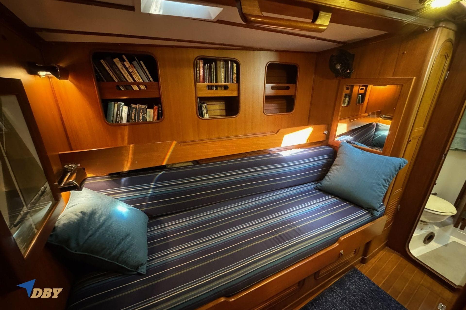 Cozy cabin interior of 1983 Mason 53 yacht with striped cushions and built-in bookshelves.