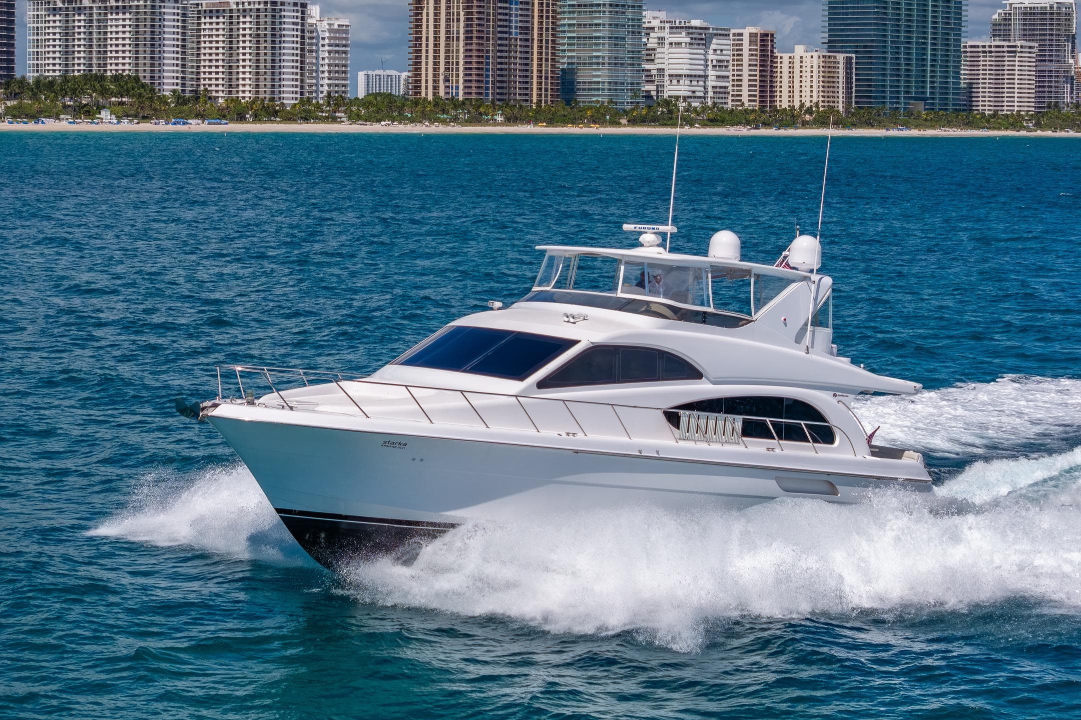 2009 Hatteras 64 Motor Yacht cruising near city skyline on blue ocean waters.