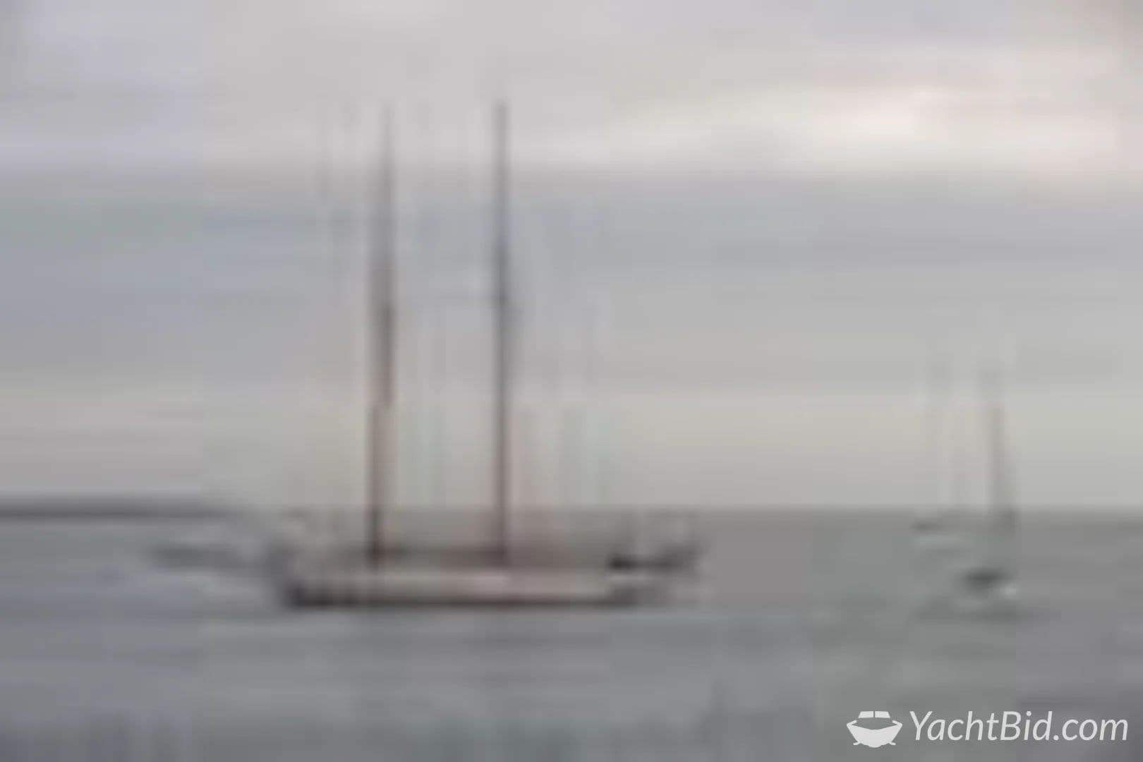 Sailing yacht on calm sea under cloudy sky.
