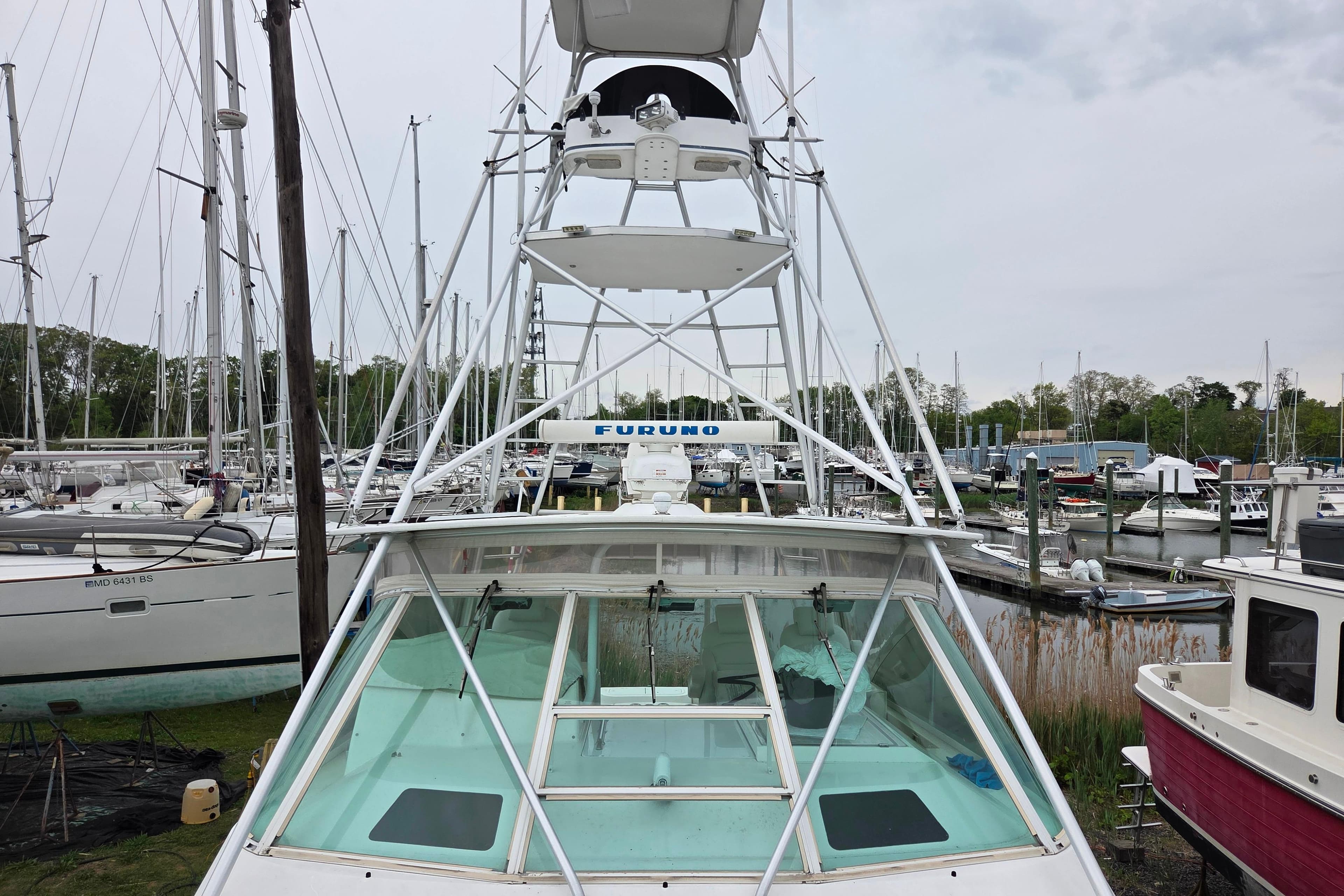 1999 Cabo 35 Express boat with tower, docked in a marina with sailboats.