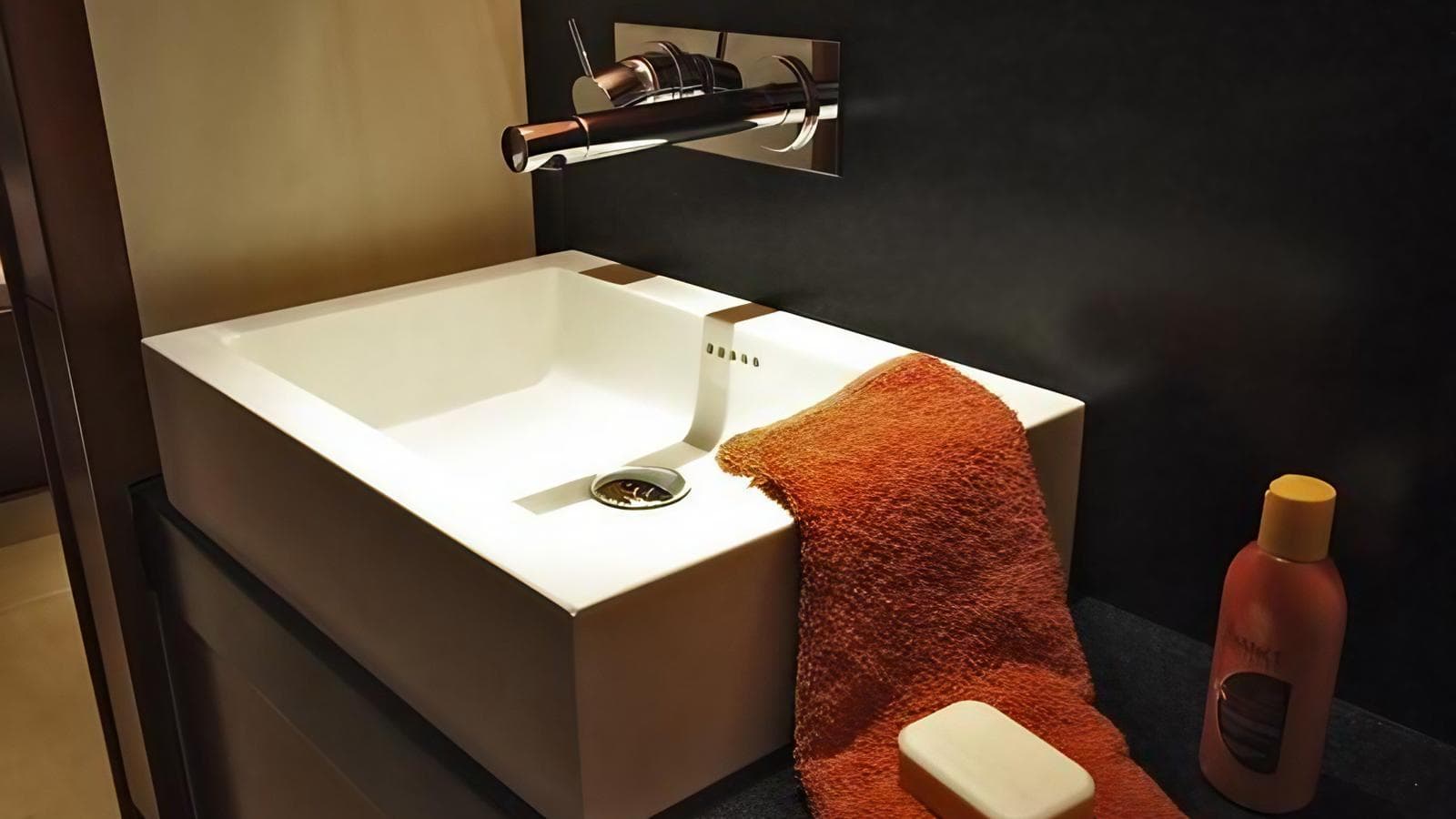 Modern bathroom sink with orange towel, soap, and lotion on a Hanse 62 yacht, 2007 model.
