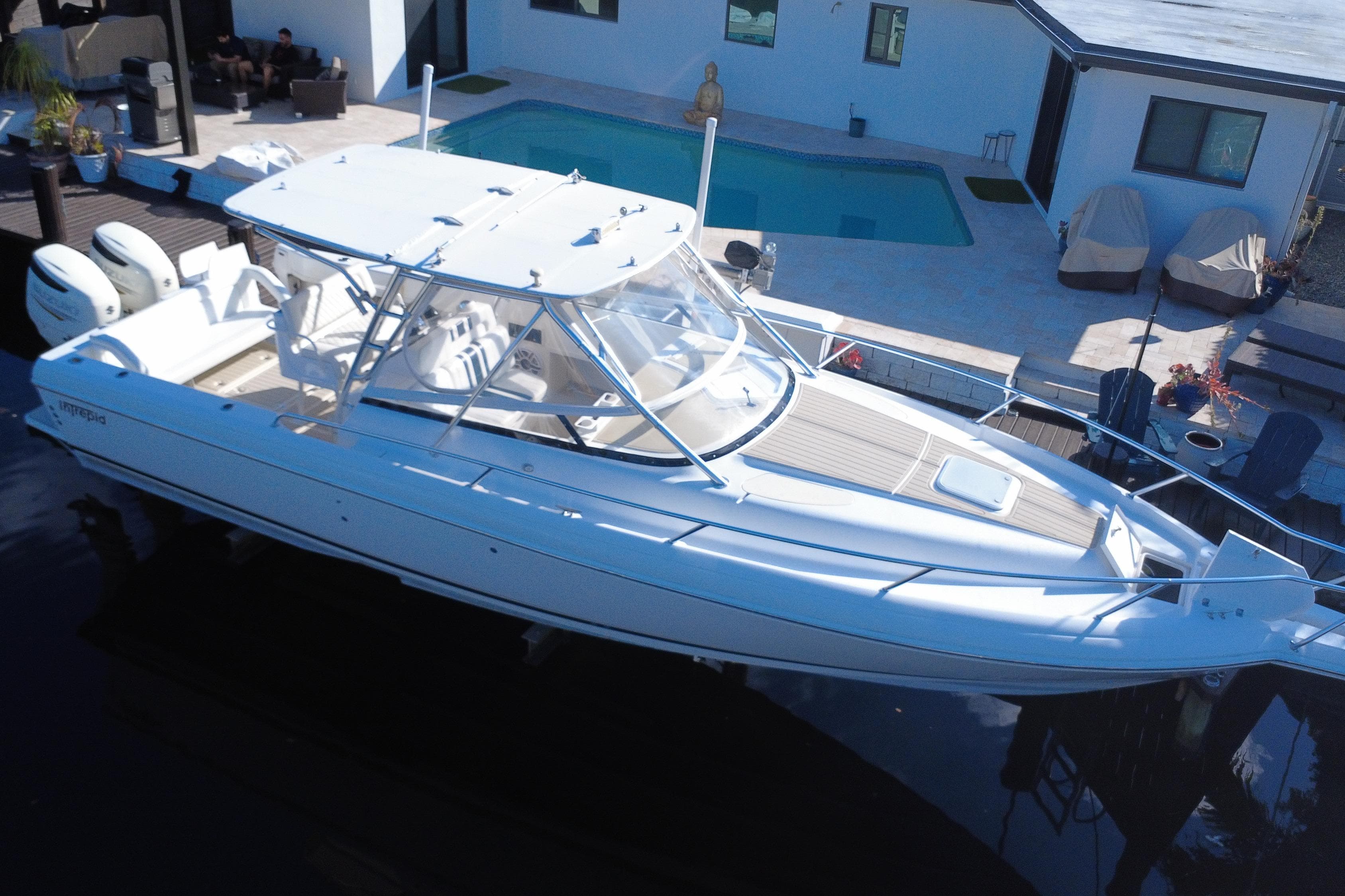 2005 Intrepid 348 Walkaround boat docked near a modern house with a pool.