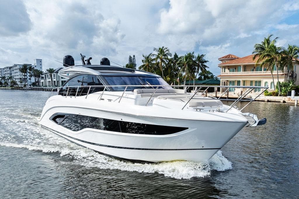 2021 Princess V55 yacht cruising on a scenic waterway with palm trees and luxury homes.