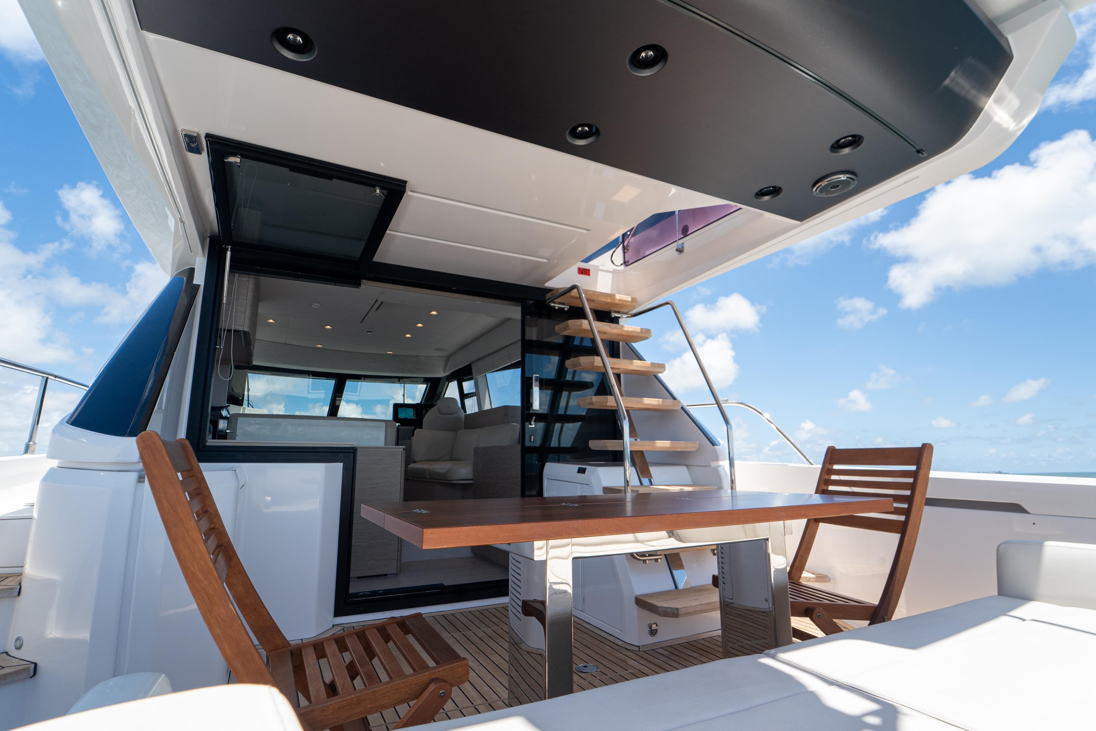 Luxurious 2022 Ferretti Yachts 500 deck with wooden chairs and table under blue sky.