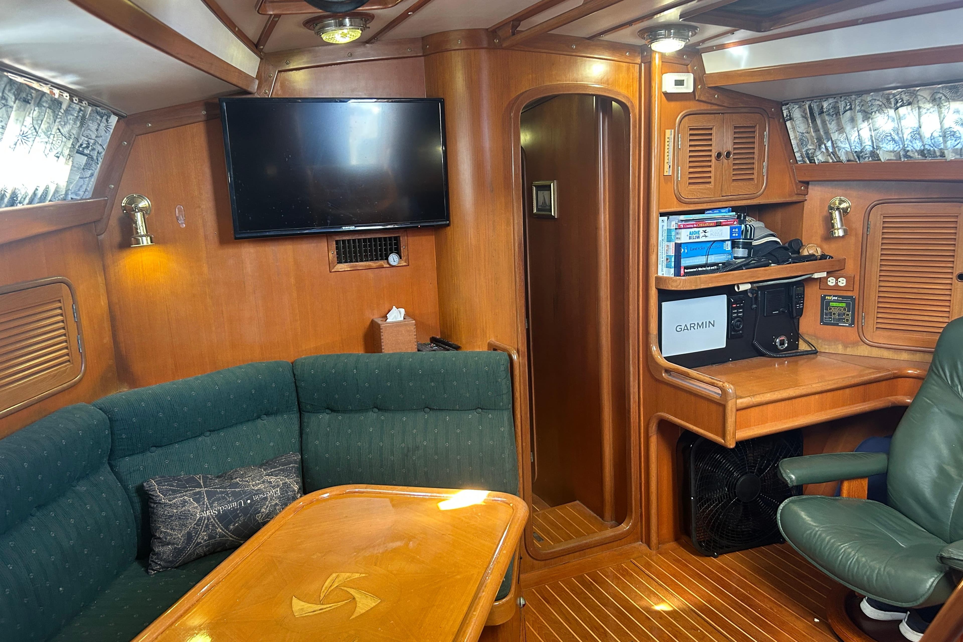 Interior of 1995 Tayana 48 yacht with wood paneling, green seating, and navigation equipment.