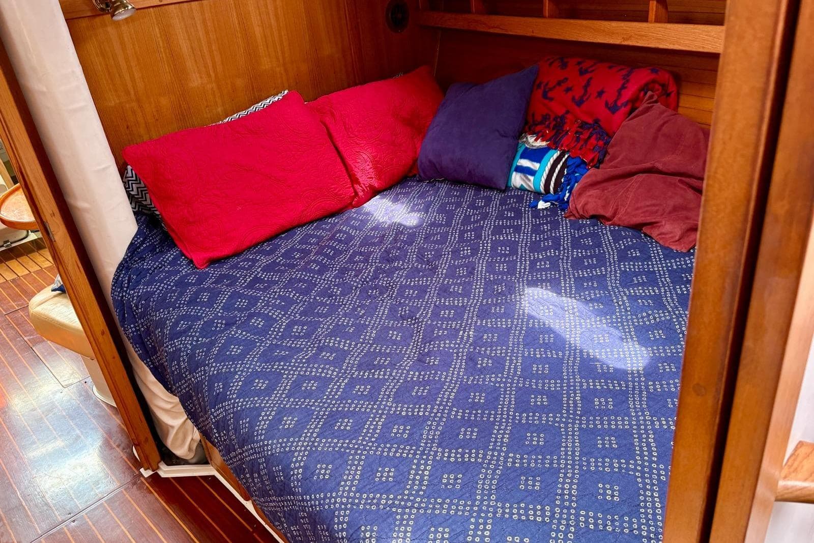 Cozy cabin bed with colorful pillows in a 2000 Catalina 42 MkII sailboat.