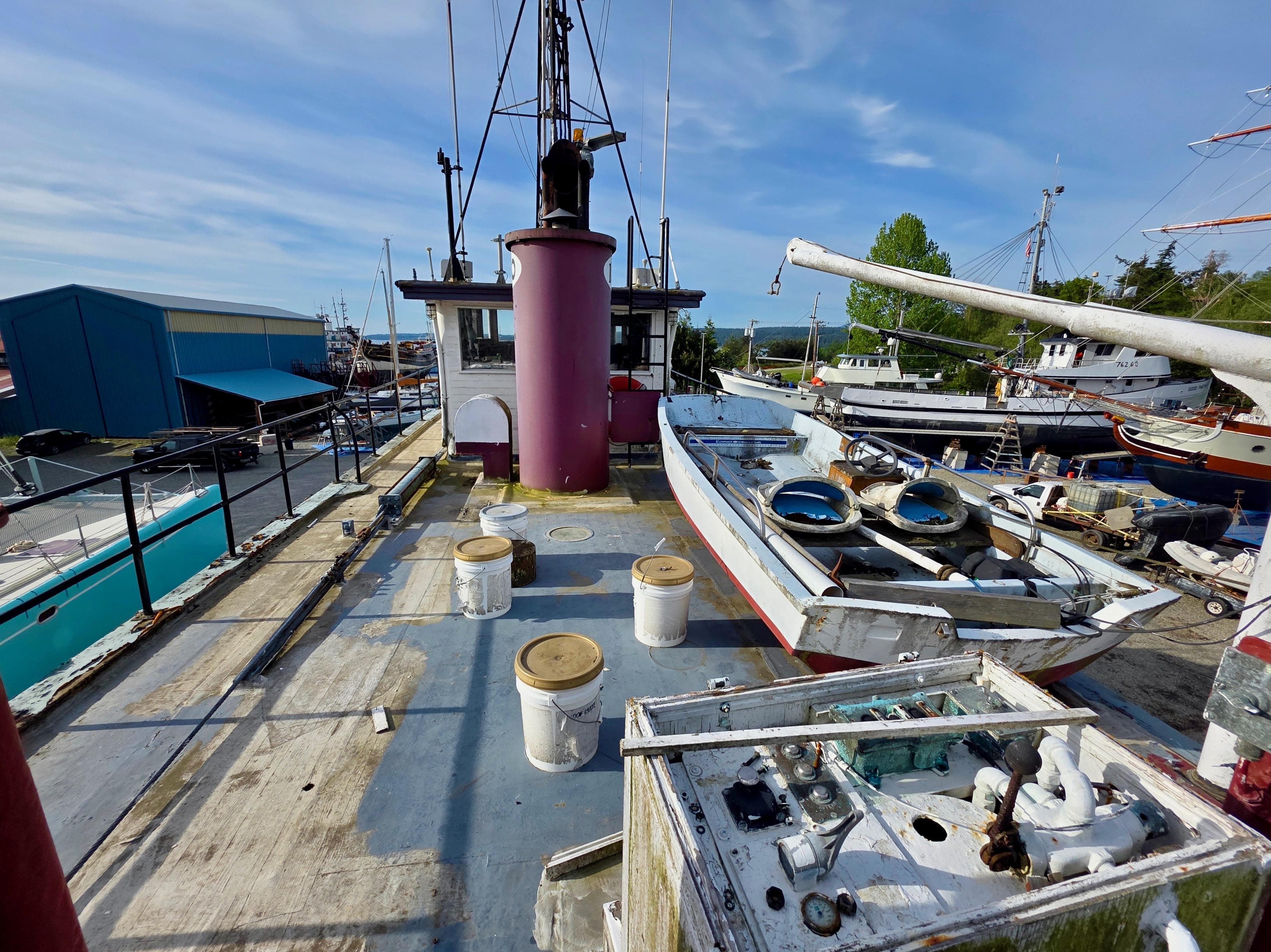 Historic 1890 custom tugboat deck with equipment, docked in a marina under a clear blue sky.