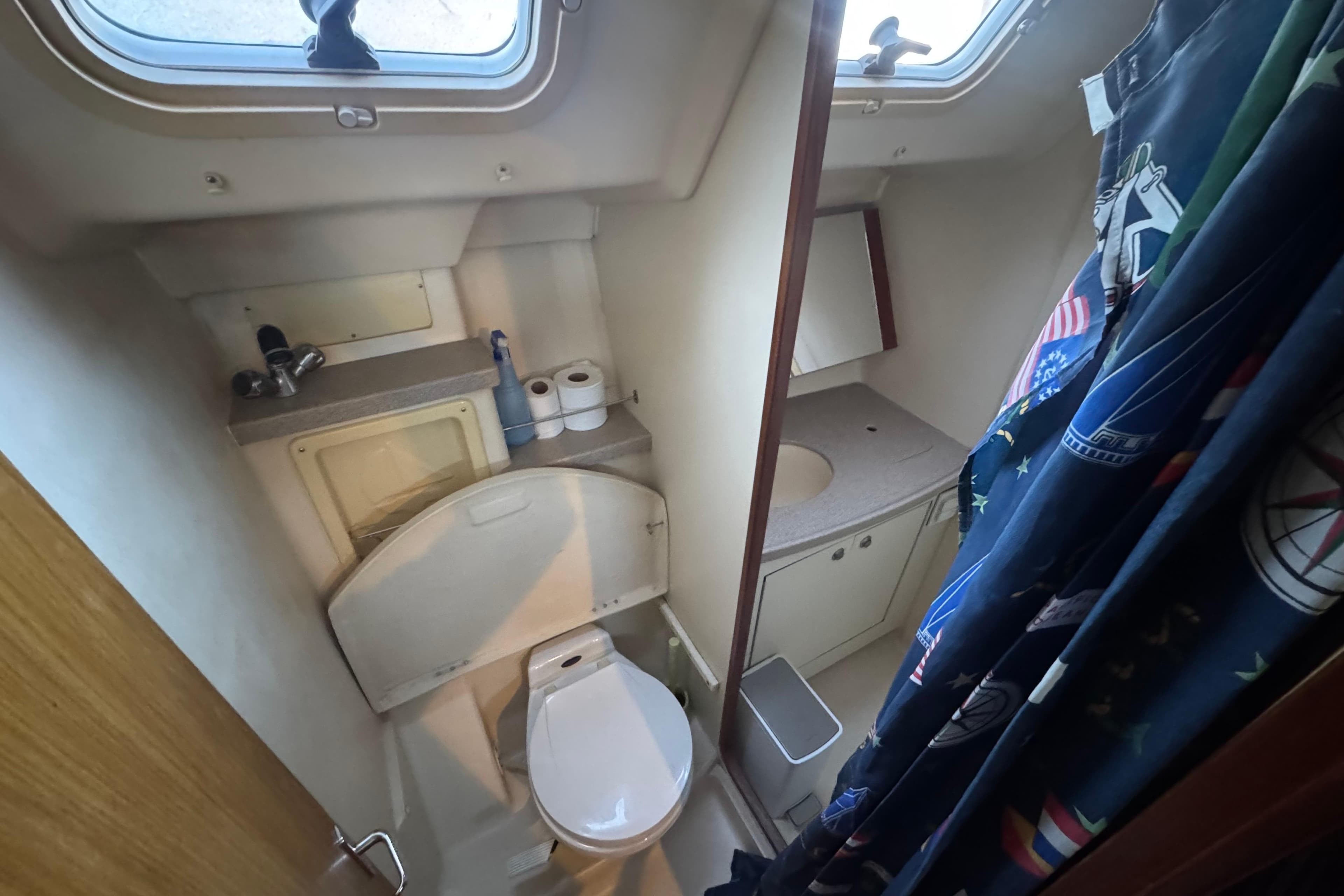 Compact bathroom in a 2000 Hunter 460 yacht with toilet, sink, and nautical-themed shower curtain.
