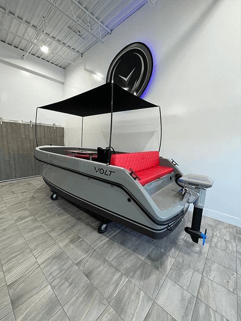 2023 Vision Marine Technologies Volt 180 boat with canopy and red seating in showroom.