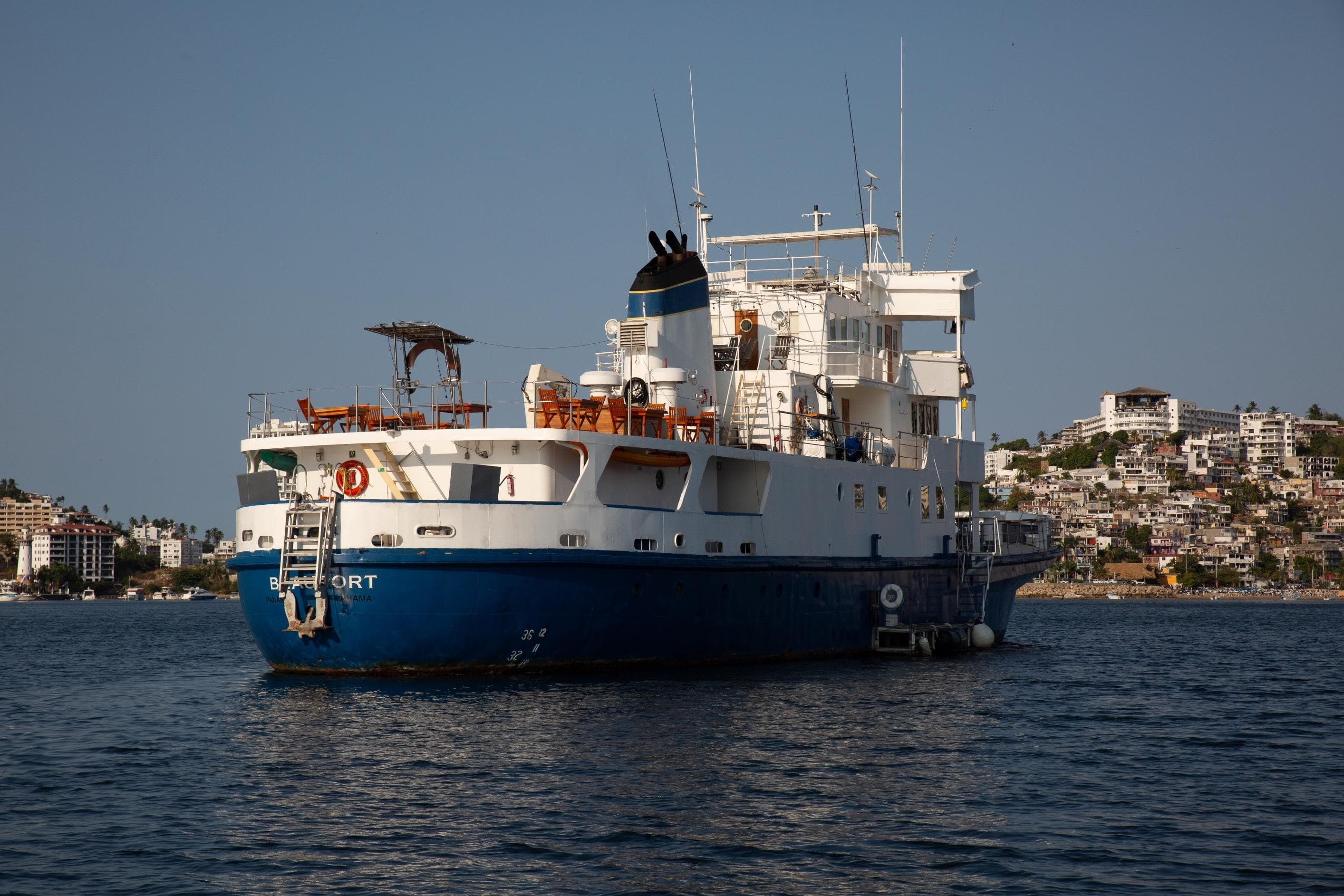 1960 custom commercial ship anchored near coastal cityscape.