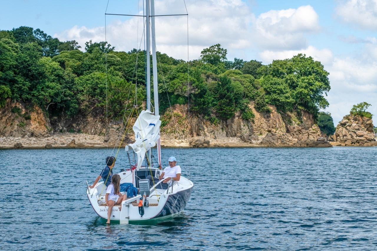 Sailing on a 2026 J Boats J/7 near rocky coastline under blue skies.