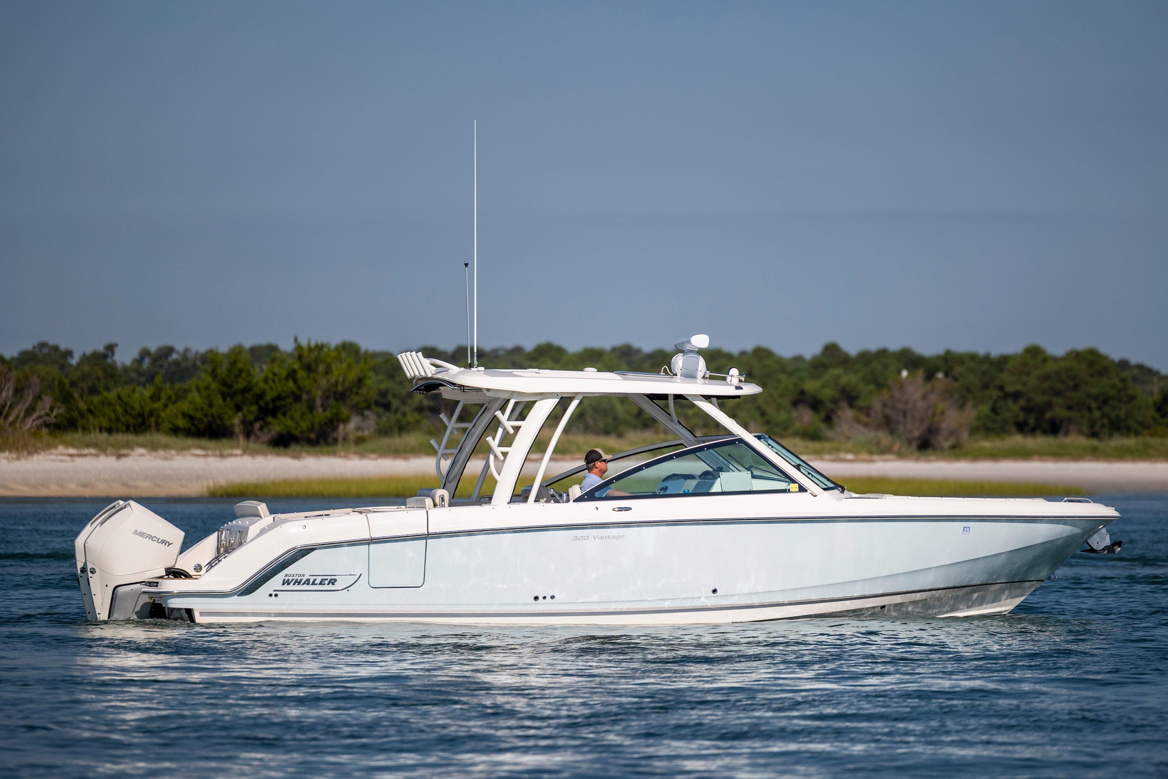 2023 Boston Whaler 320 Vantage boat cruising on calm water near a scenic shoreline.