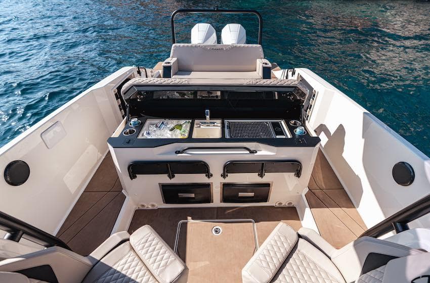 2025 Navan S30 boat interior with outdoor kitchen and seating, on clear blue water.
