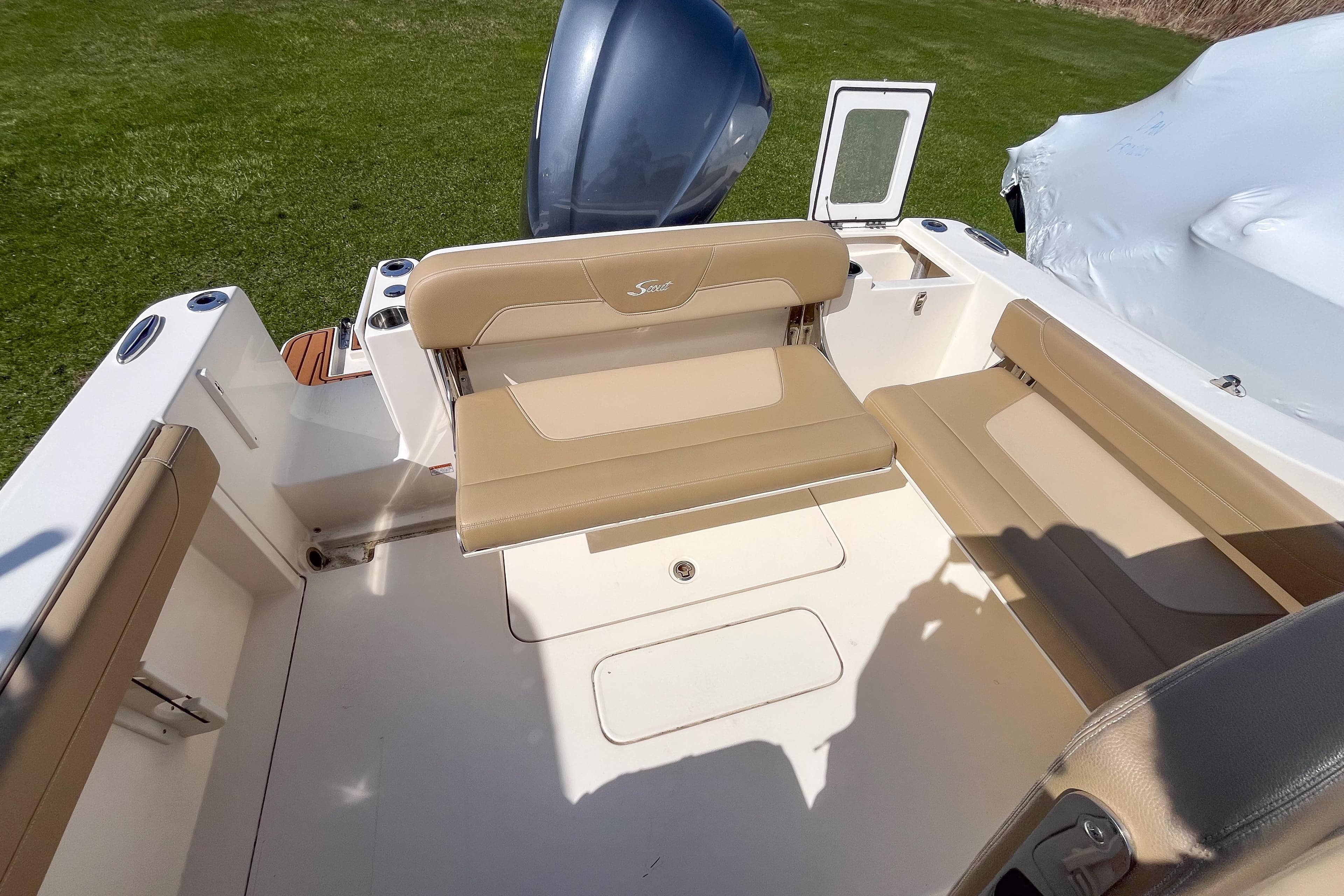2021 Scout 240 Dorado boat interior with beige seating and motor, parked on grass.