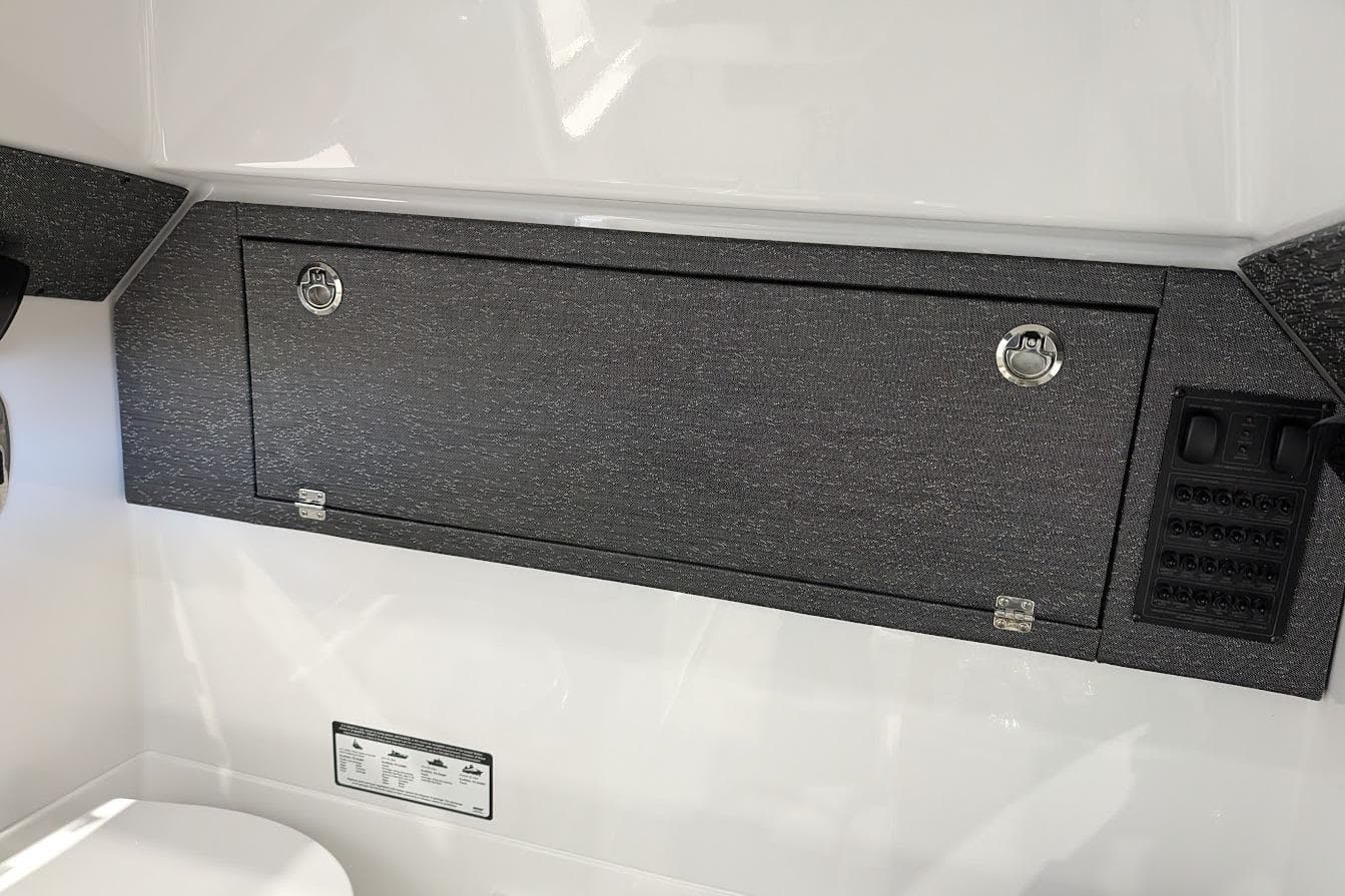 Interior view of 2026 Monterey Elite 25 OB boat with storage compartment and control panel.