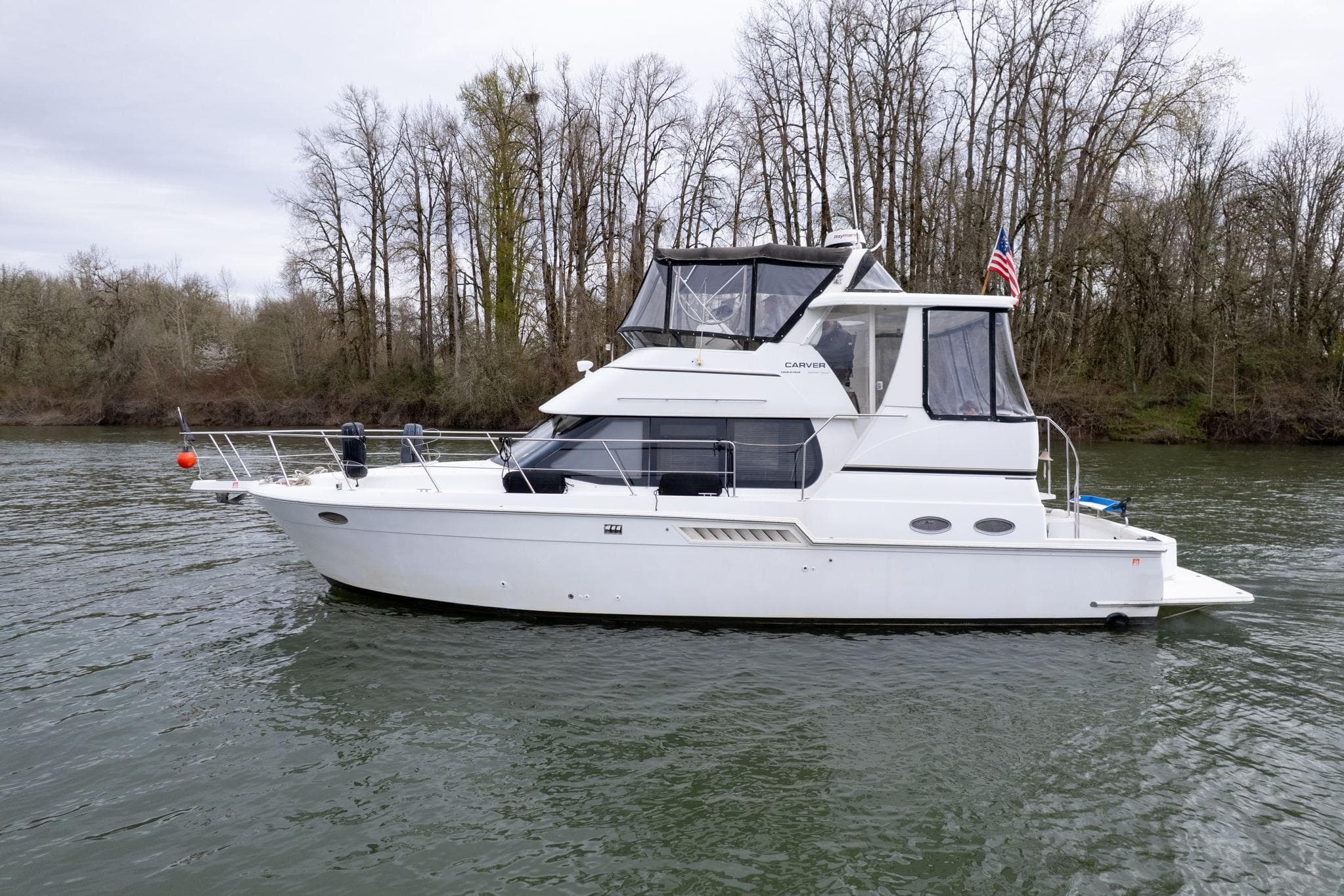 2000 Carver 404 Cockpit Motor Yacht on a serene river with forested background.