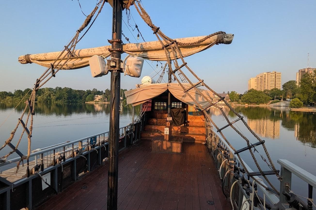 Custom 2016 pirate ship on calm river, surrounded by trees and buildings.
