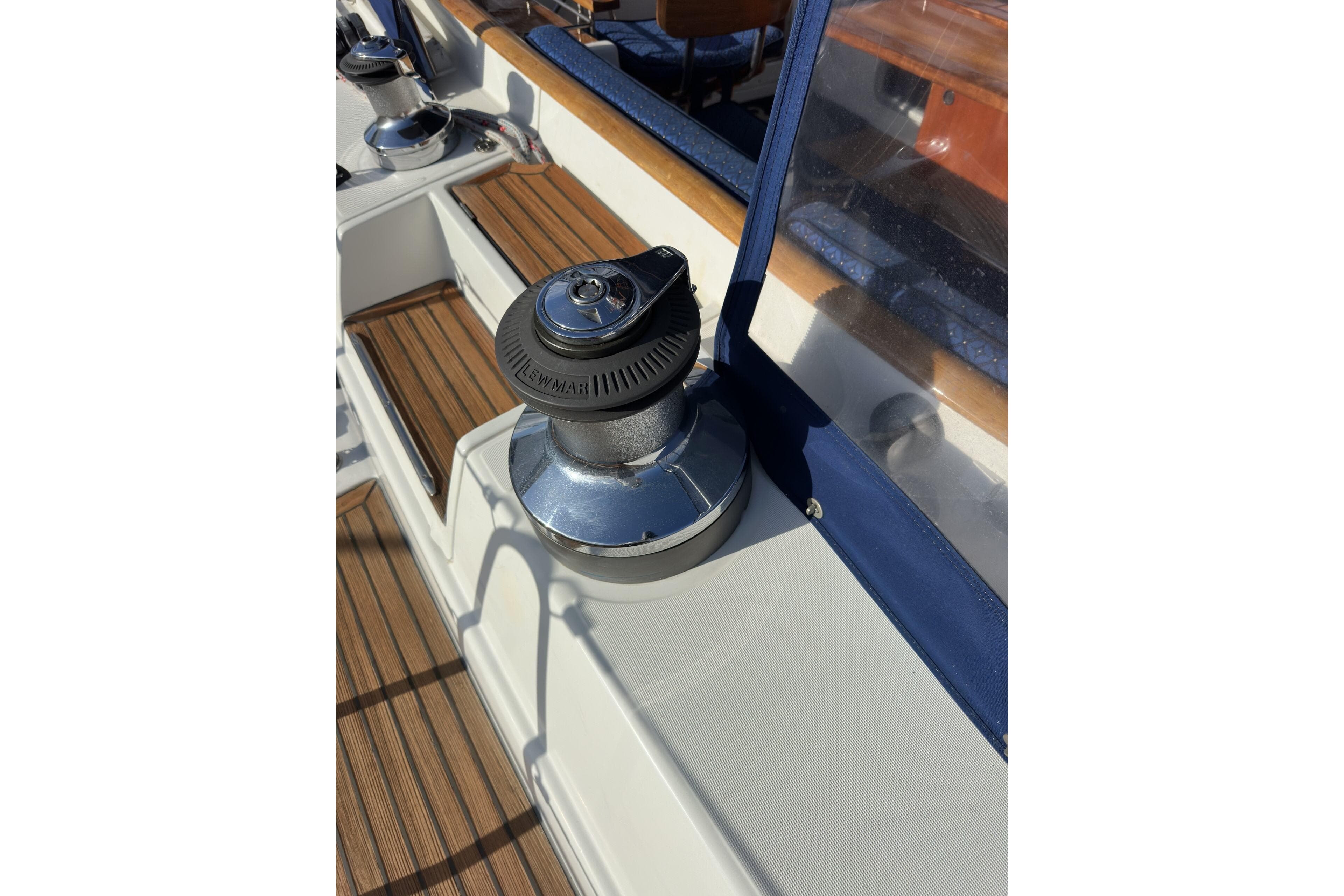 Winch on deck of 2003 Beneteau 57 sailboat, featuring teak flooring and blue trim.