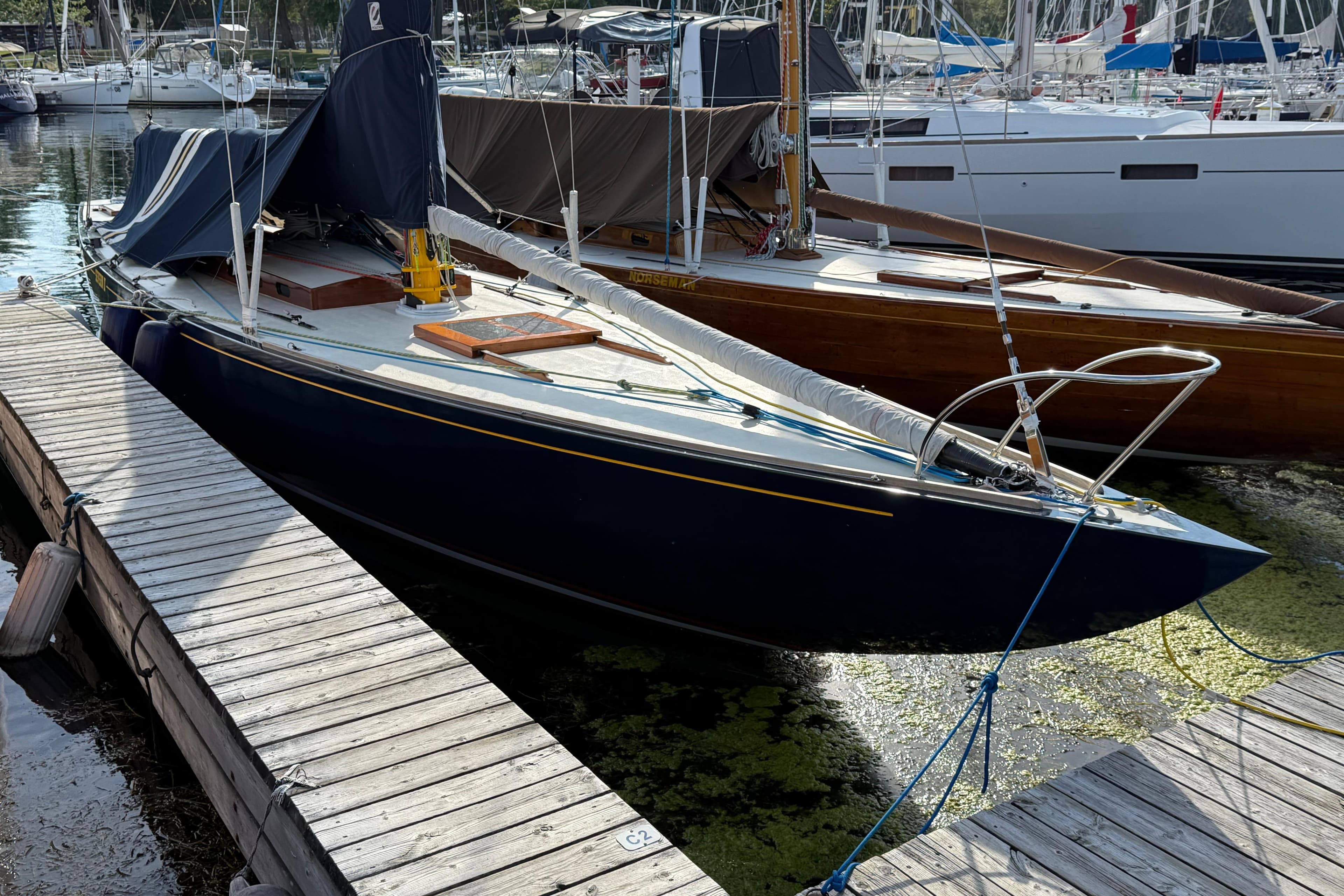 Vintage 1934 International 8mR sailboat docked at marina, surrounded by other boats.