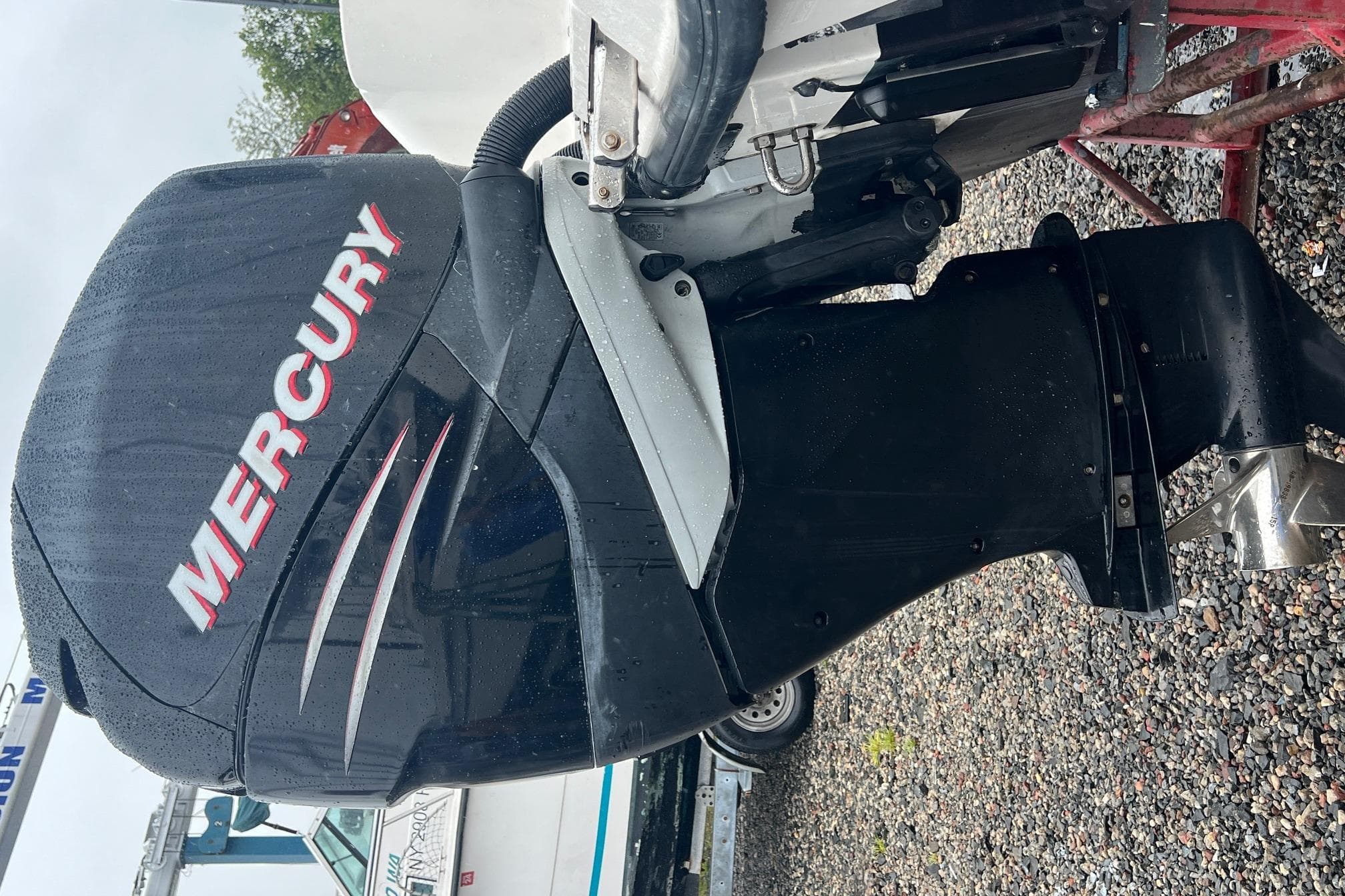Mercury outboard motor on a 2005 Boston Whaler 305 Conquest, parked on gravel.