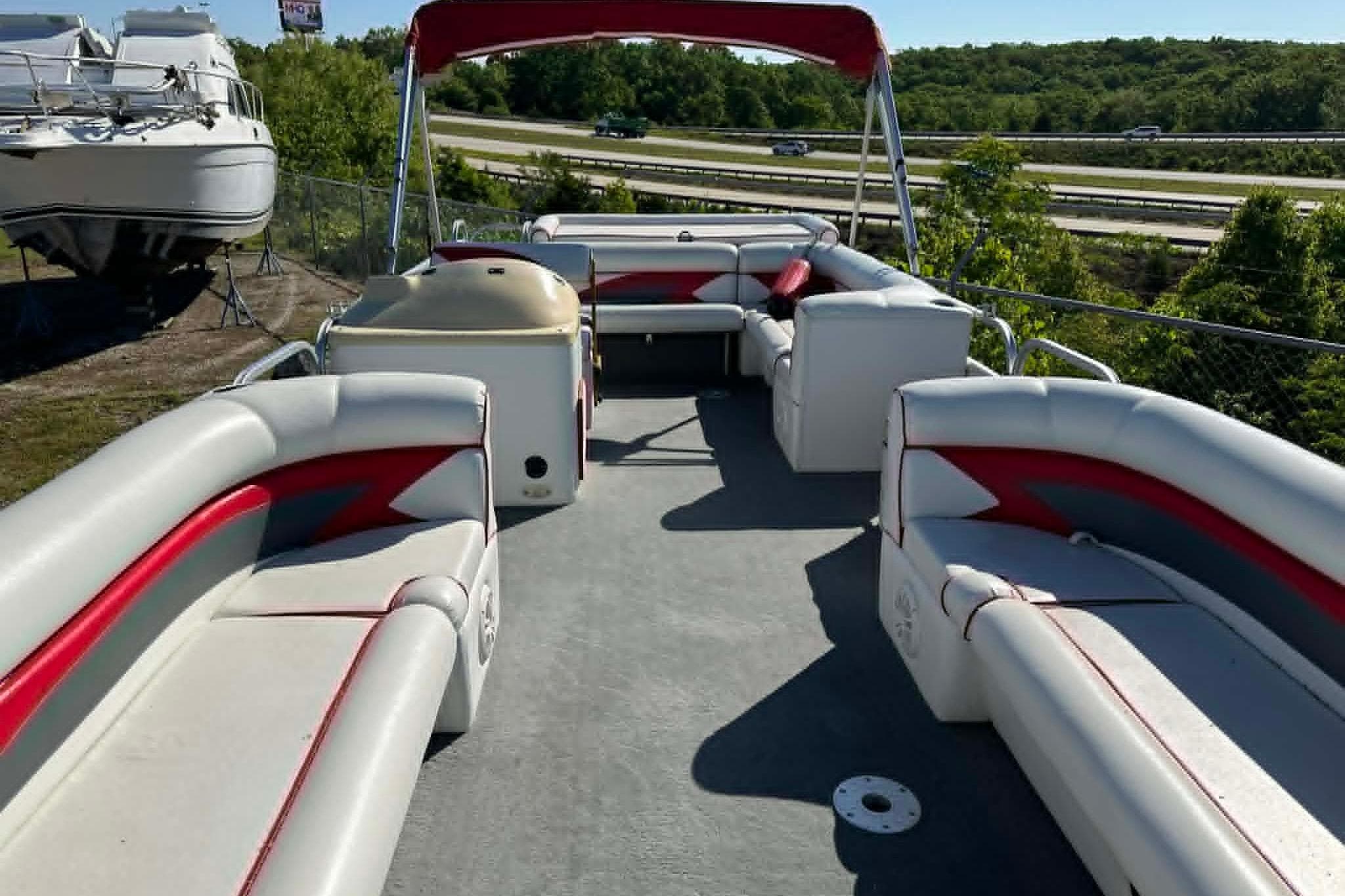 1999 PlayCraft Sport 2400 pontoon boat with red and white seating, docked outdoors.