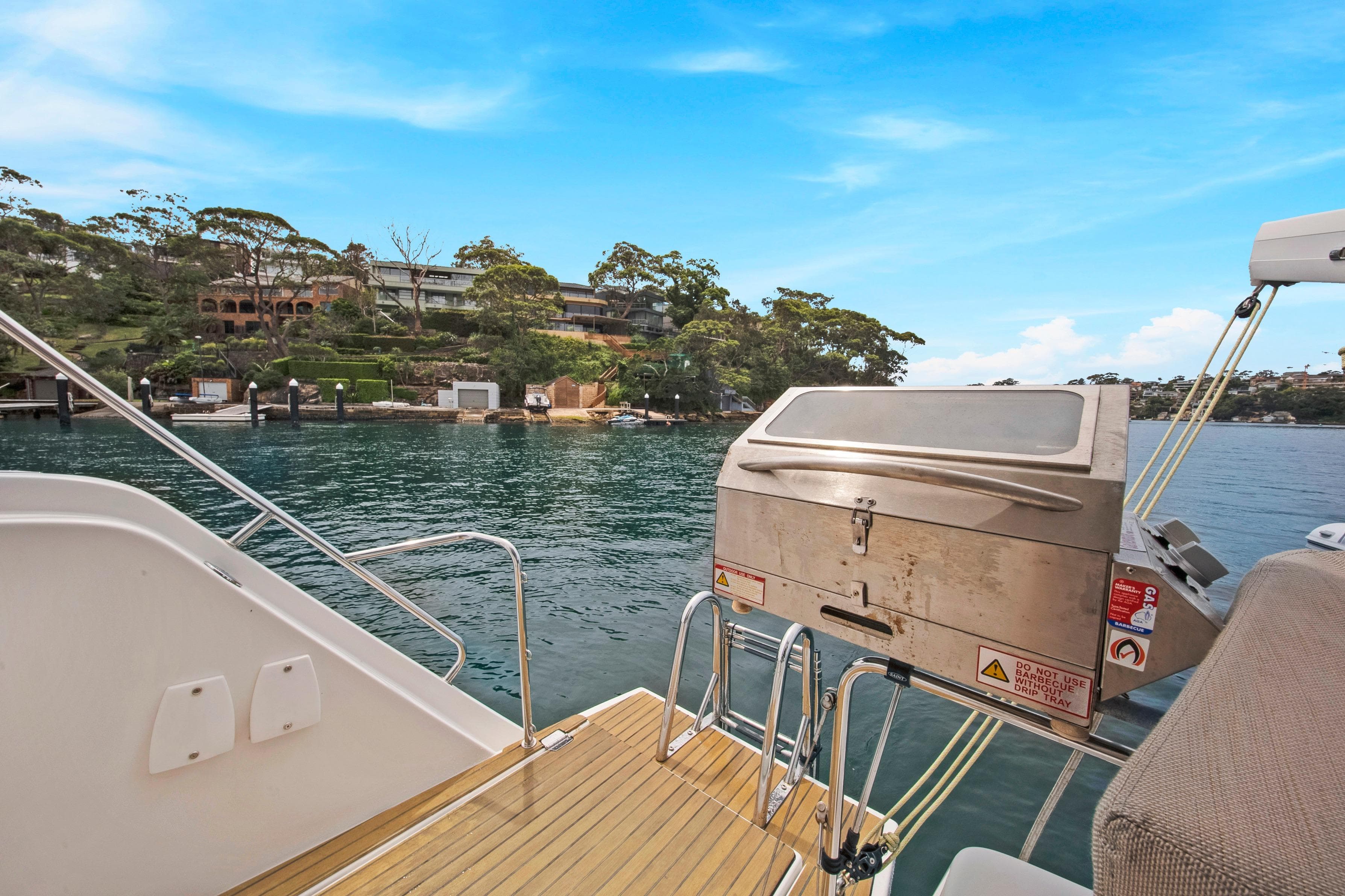 Aventura 37 yacht deck with barbecue grill, overlooking serene waterfront and lush greenery, 2023 model.