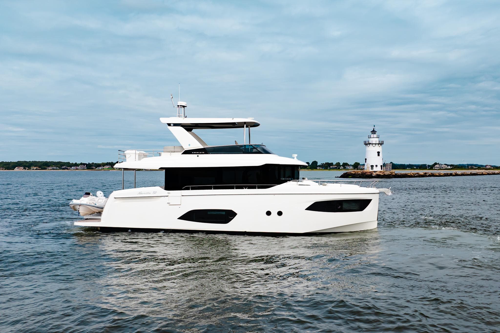 2023 Absolute 52 Navetta yacht cruising near a lighthouse on a calm sea.