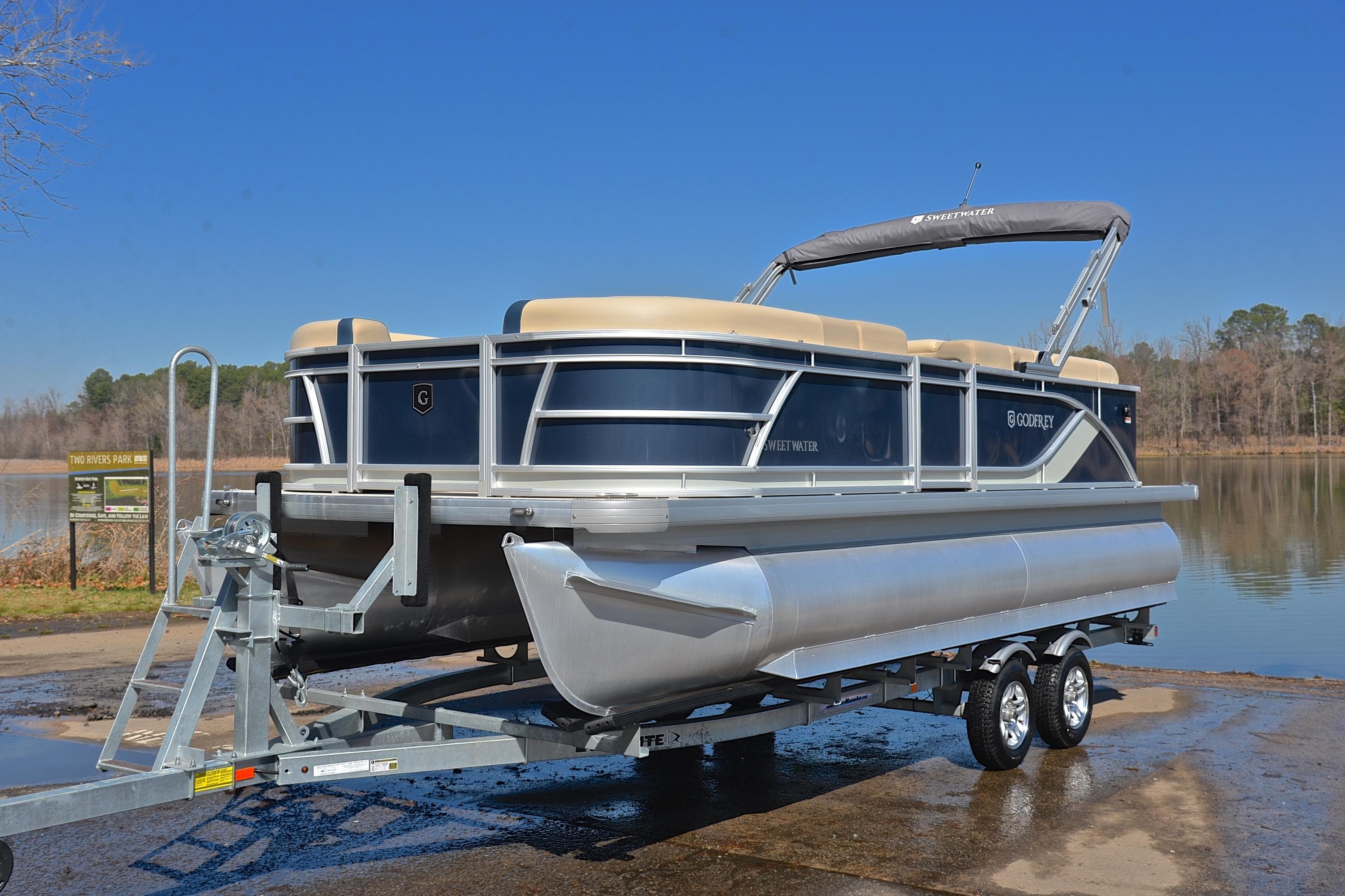 2025 Godfrey Sweetwater 2086 C pontoon boat on trailer by a lake.