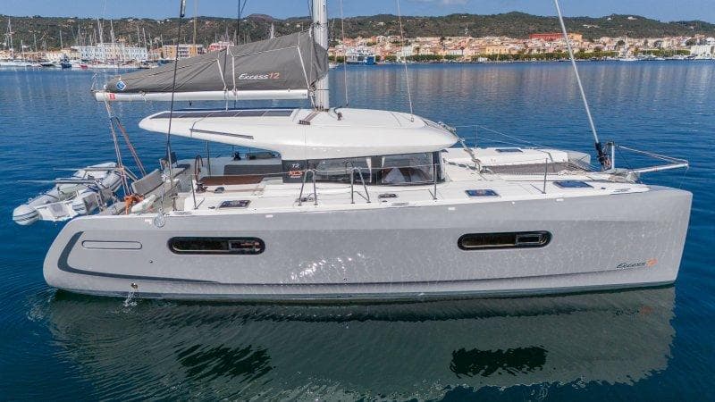 2022 Excess 12 catamaran sailing on calm waters near a coastal town.