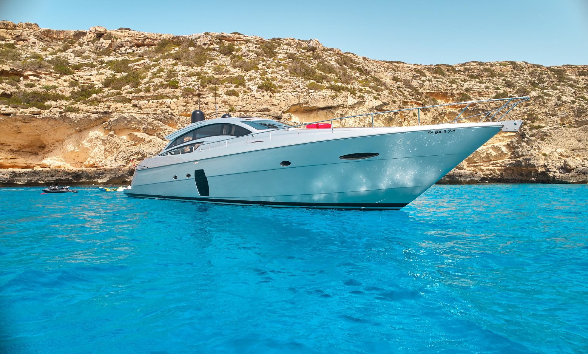 Luxury 2007 Pershing 72 yacht anchored in clear blue waters near rocky coastline.