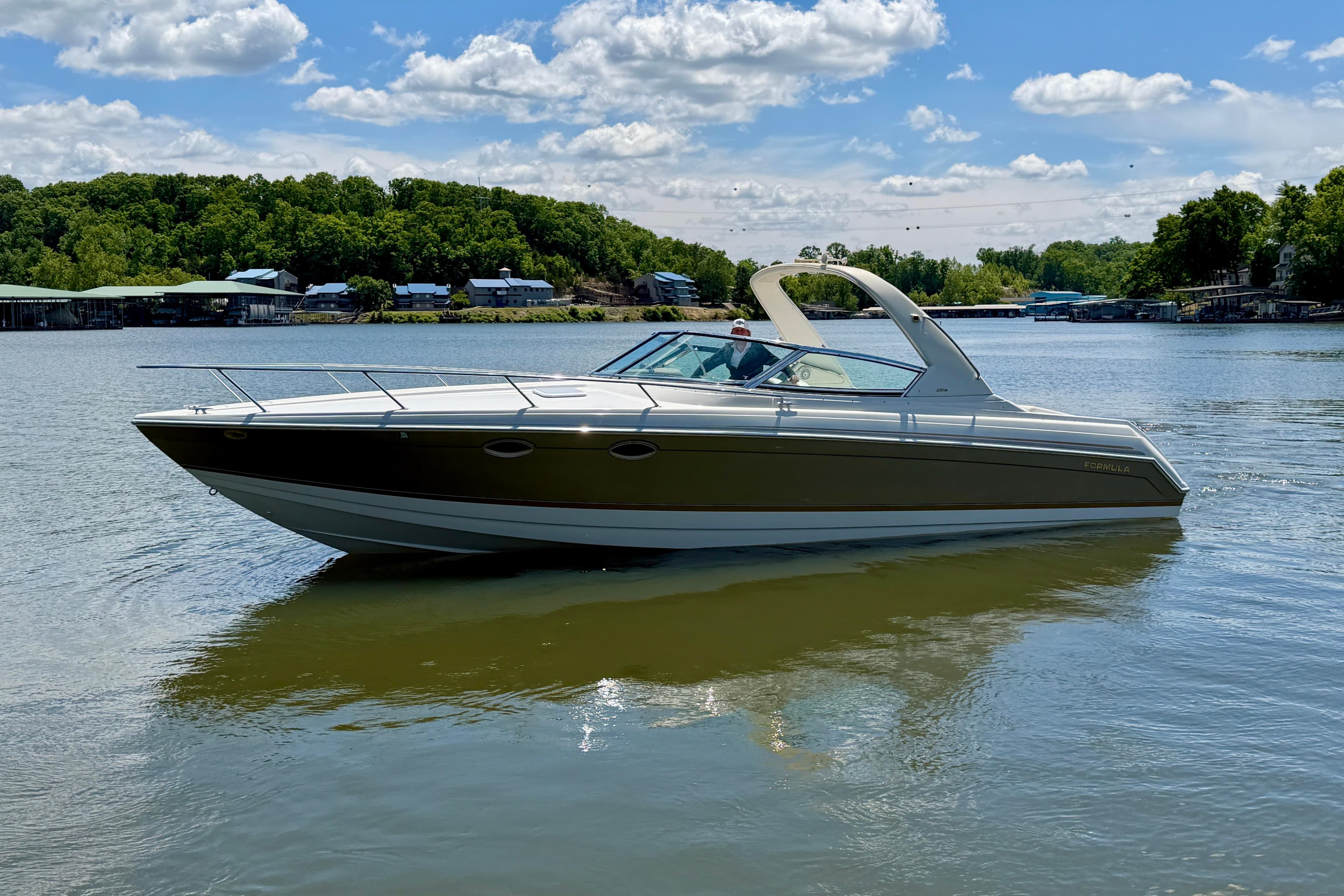 2003 Formula 330 Sun Sport boat on a serene lake with lush green shoreline.