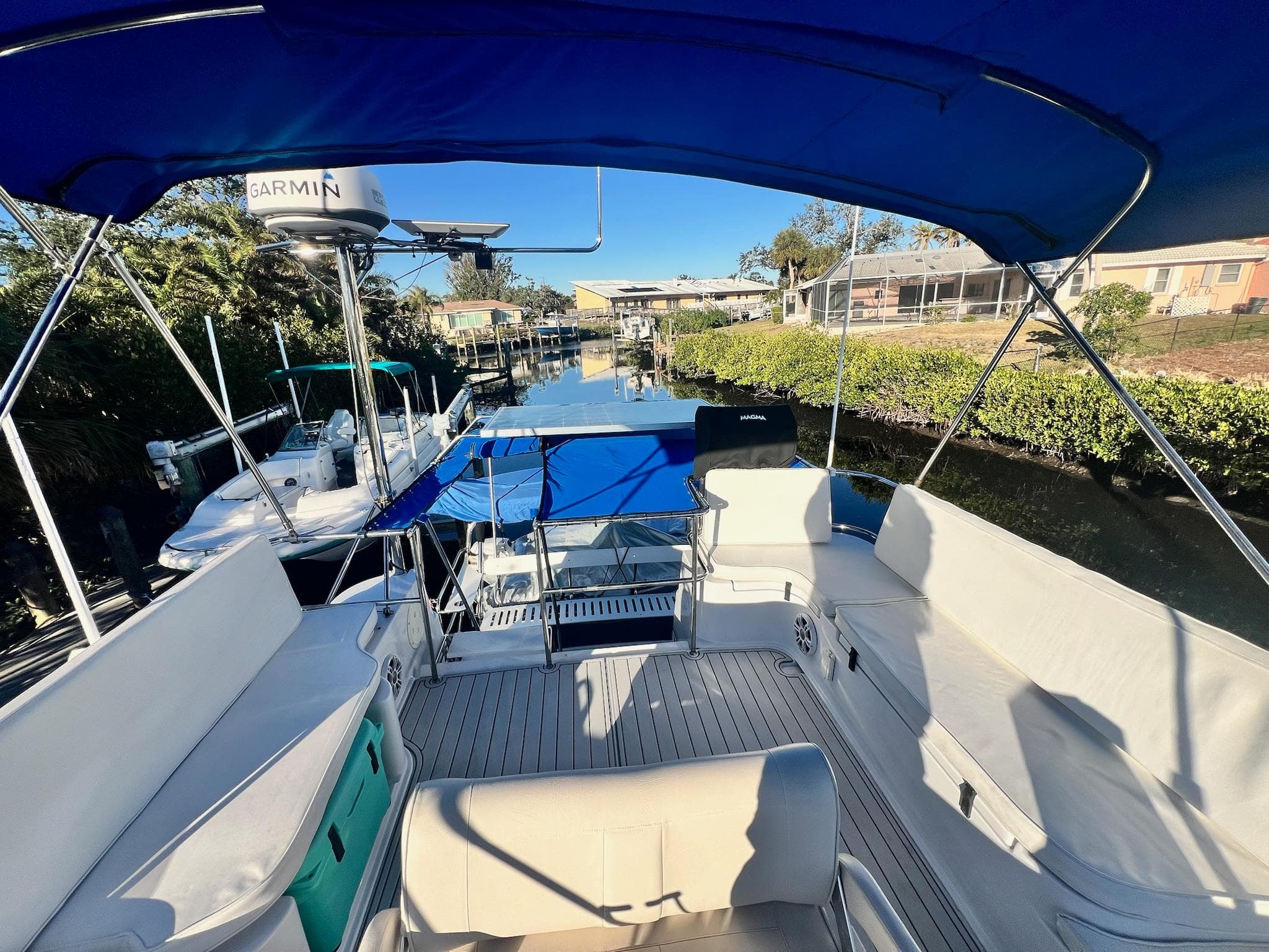 PDQ MV34 2006 boat with blue canopy, docked in a sunny marina.