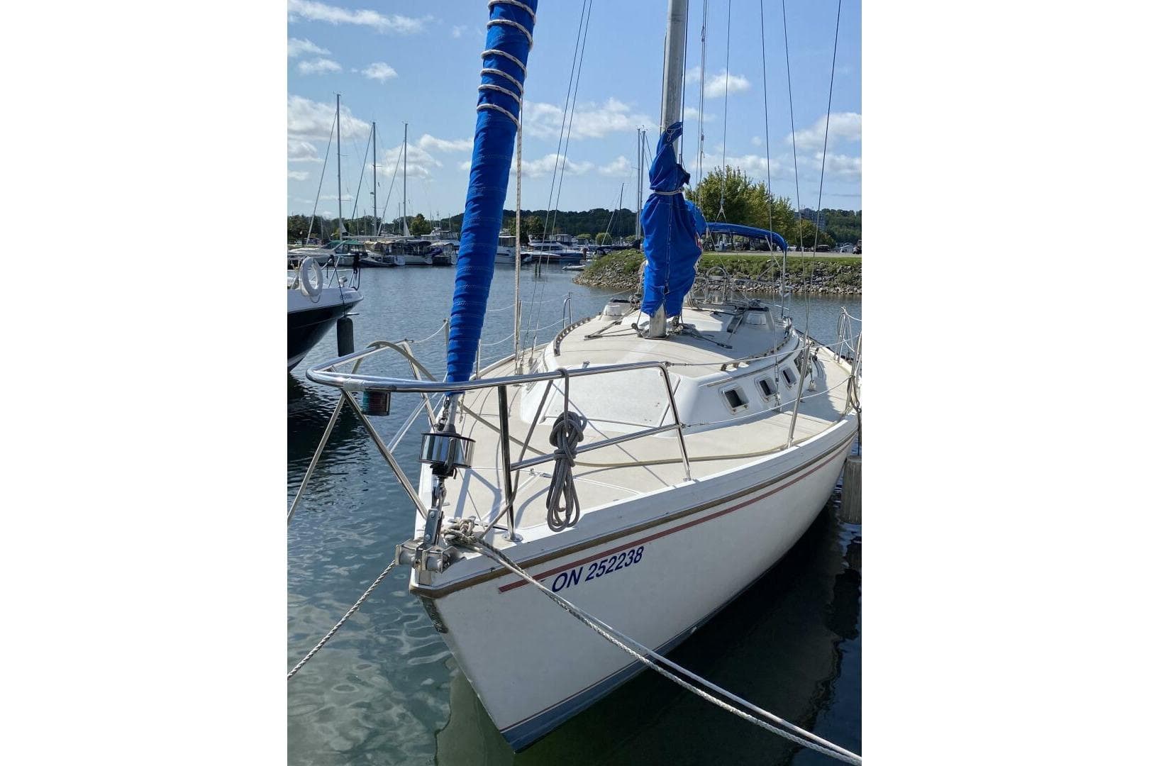 1986 Catalina 34 sailboat docked in marina, blue sail cover, calm water, clear sky.