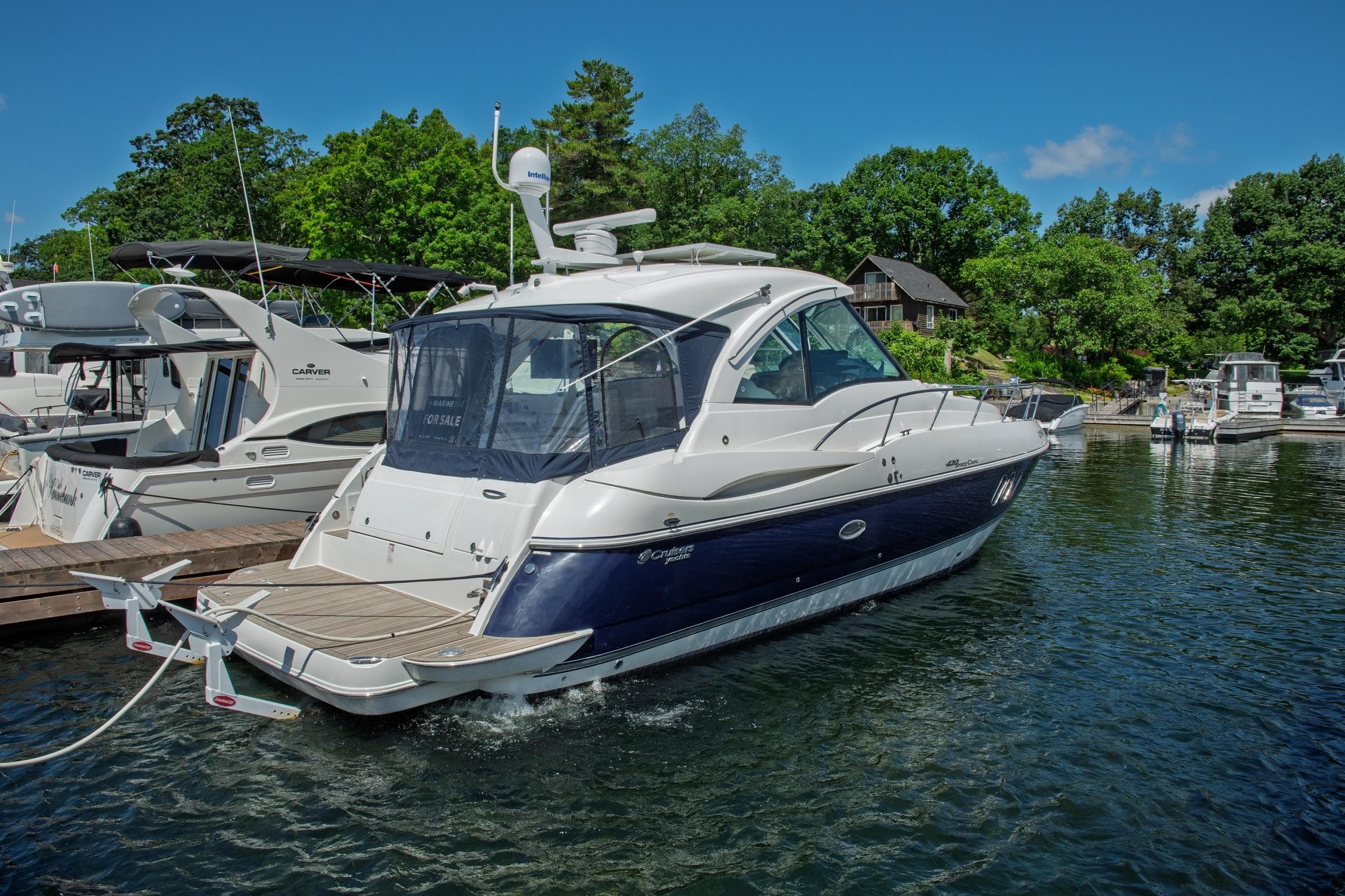 2011 Cruisers Yachts 420 Sport Coupe docked in a marina, surrounded by lush greenery.
