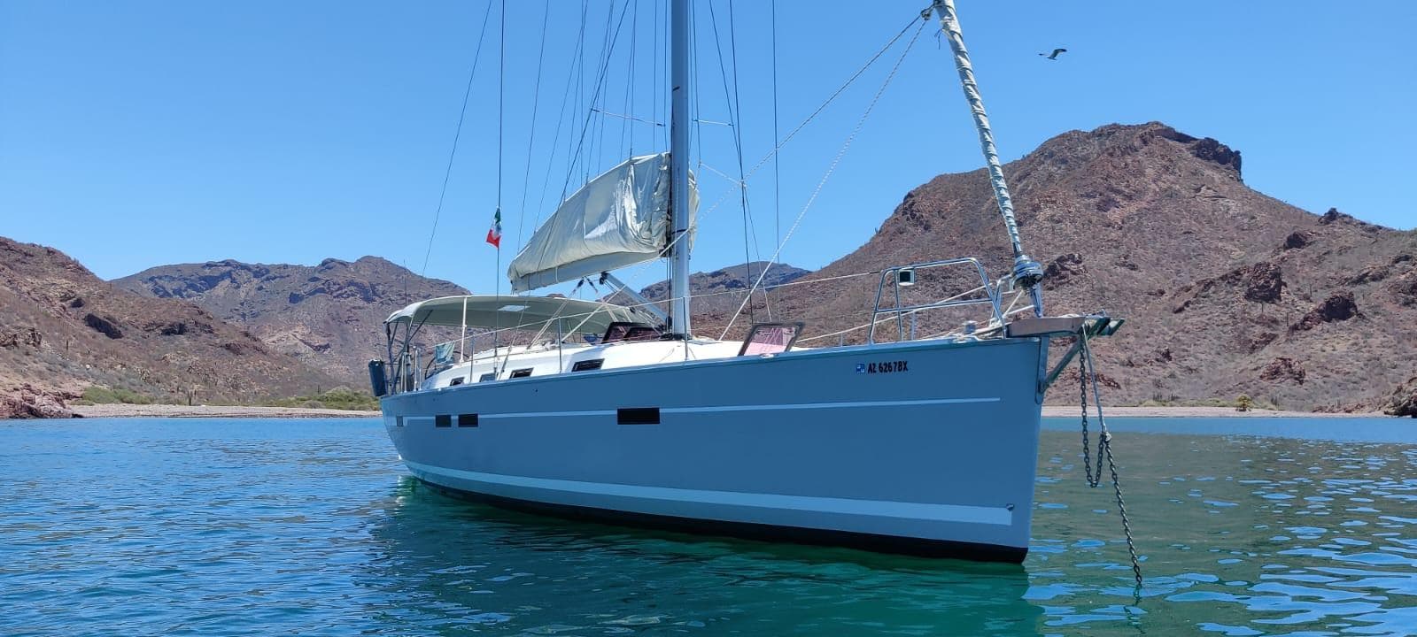 Sailing yacht Bavaria 45 (2011) anchored in scenic bay with mountainous backdrop.