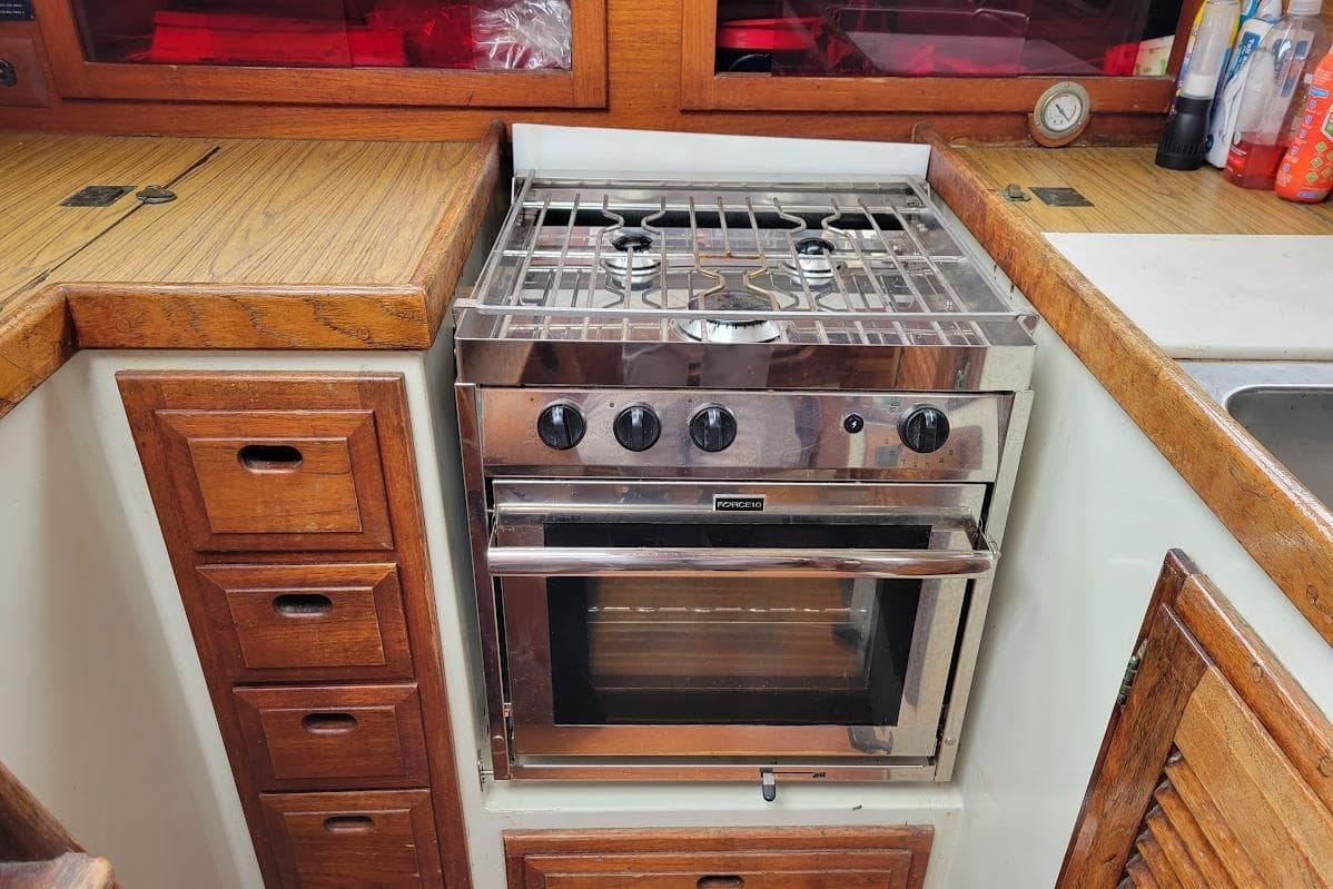 Vintage yacht kitchen with stainless steel stove, wooden cabinetry, and countertop.