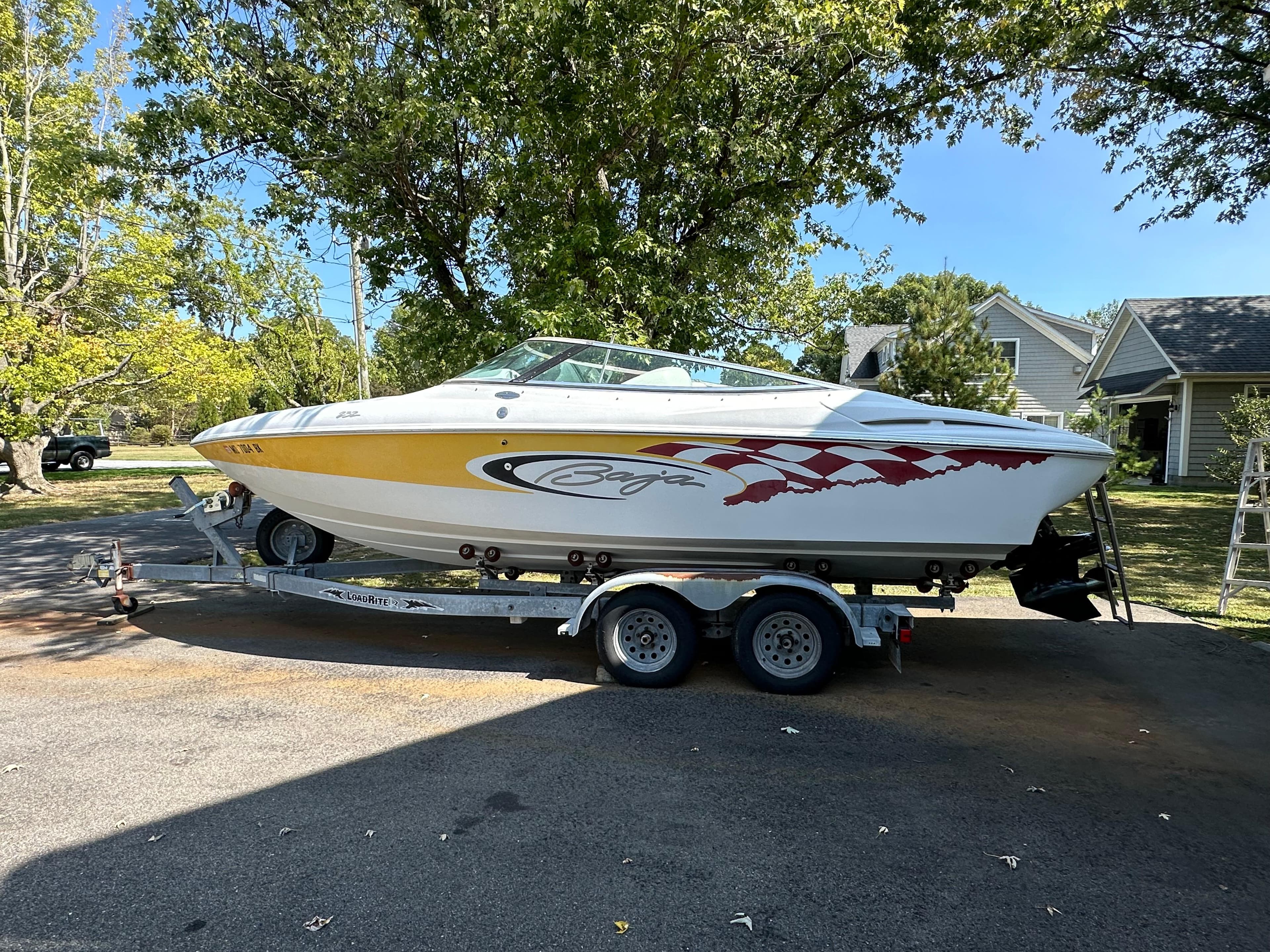 2001 Baja 232 speedboat on trailer, parked outdoors, with vibrant graphics and clear blue sky.