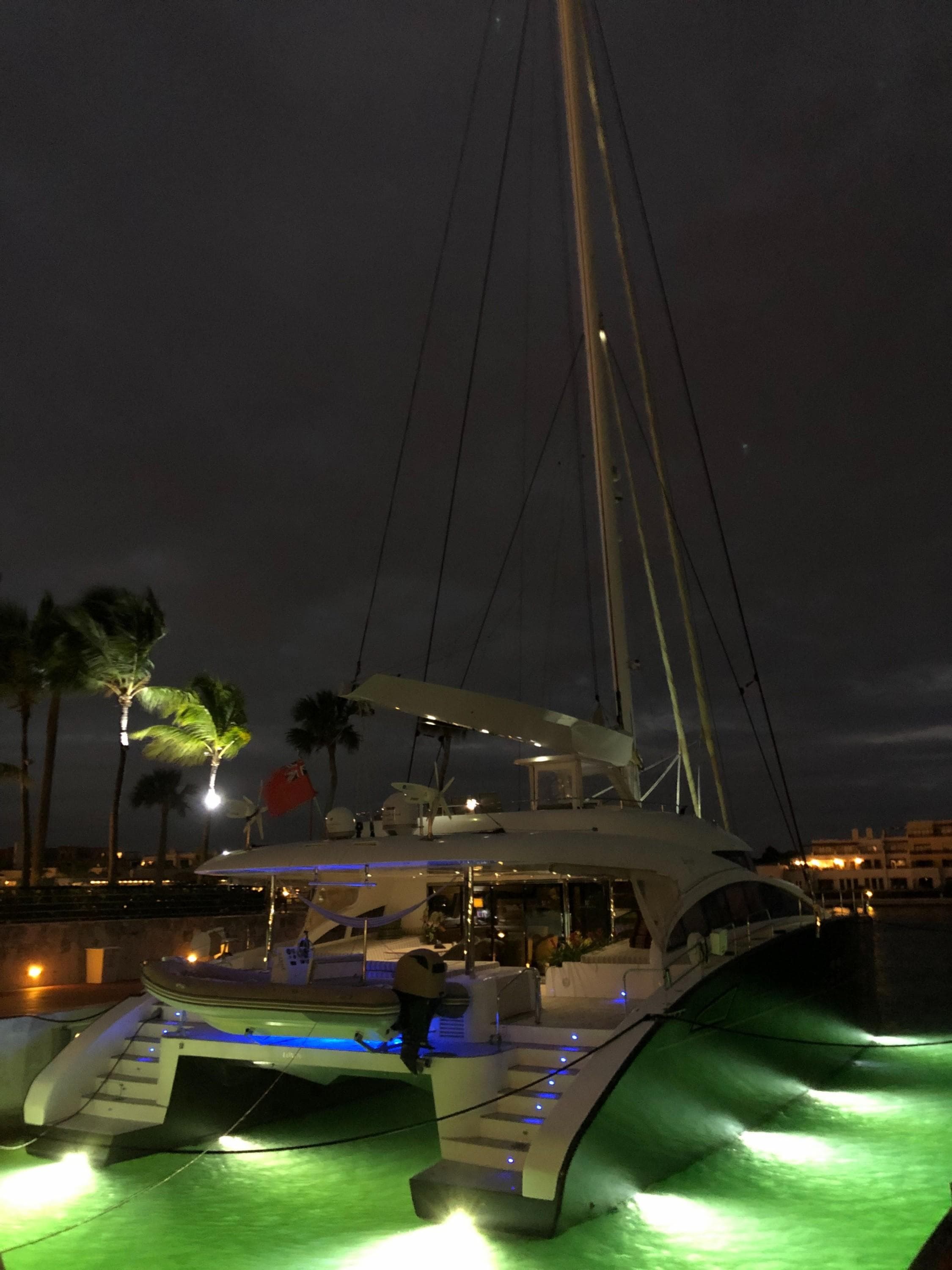 Luxurious 2012 Sunreef 82 DD yacht illuminated at night, docked with glowing green water.