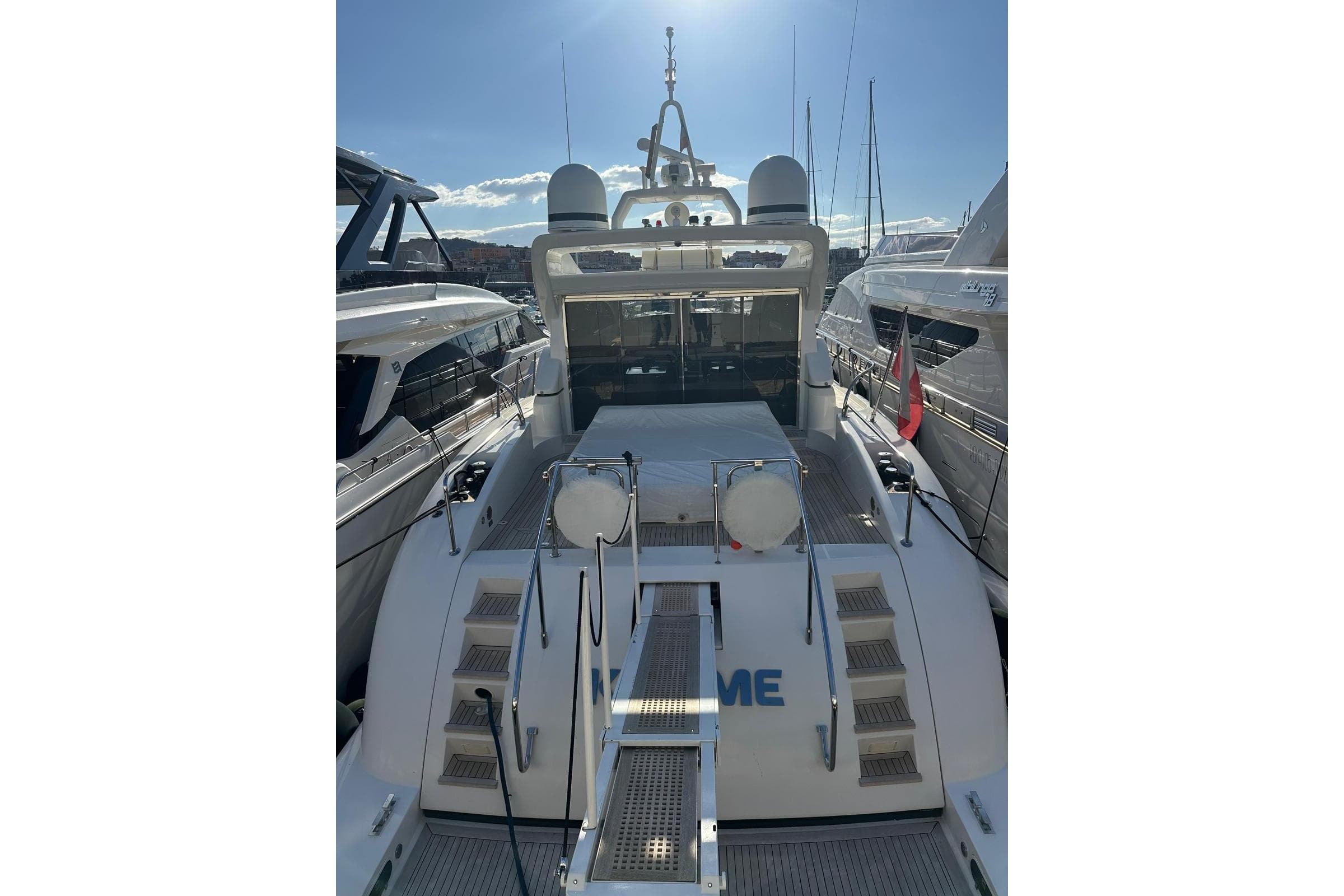 Luxury 2004 Mangusta 72 yacht docked, rear view with sunlit deck and flag.
