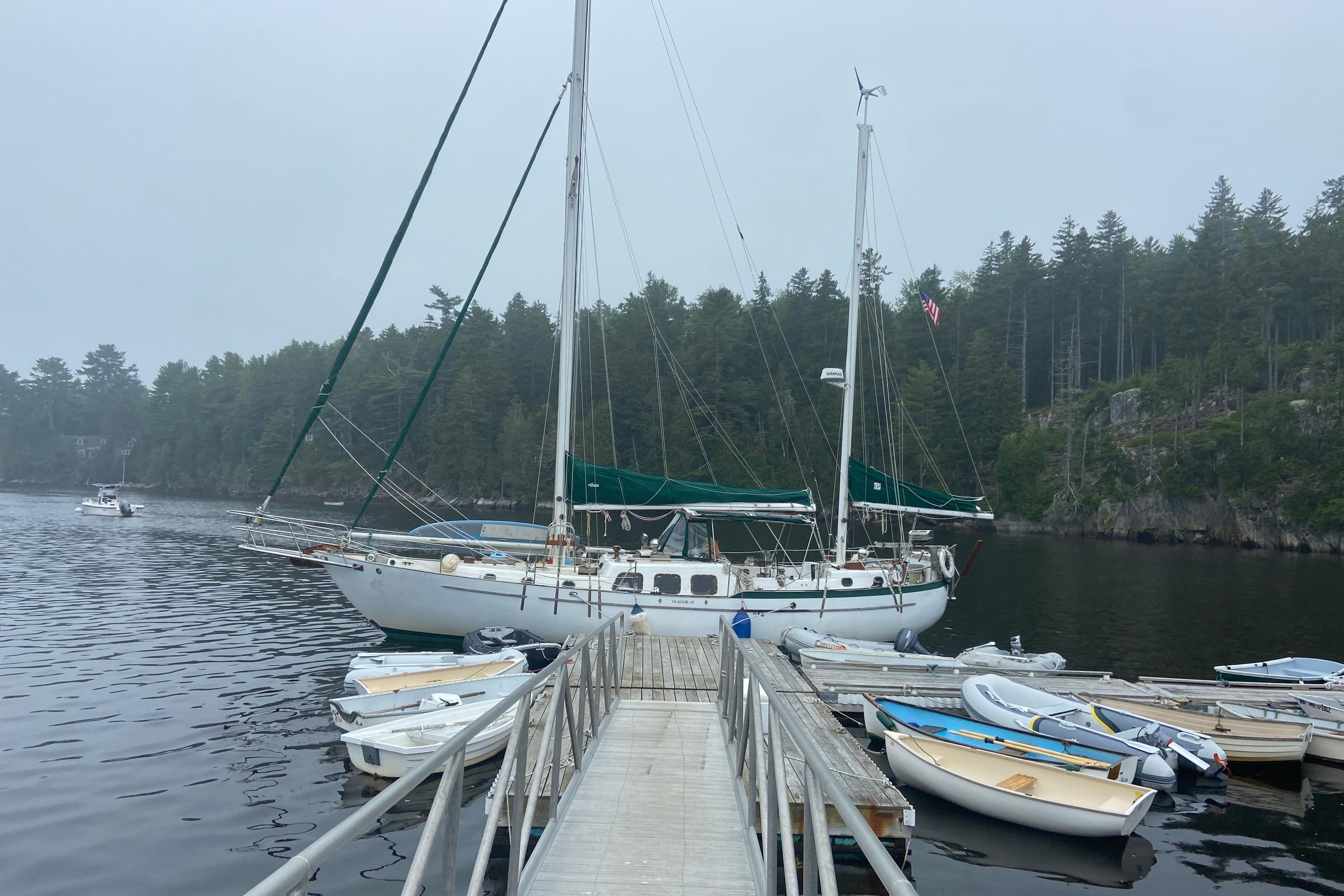 1975 Westsail Staysail Ketch docked in a serene, forested marina.