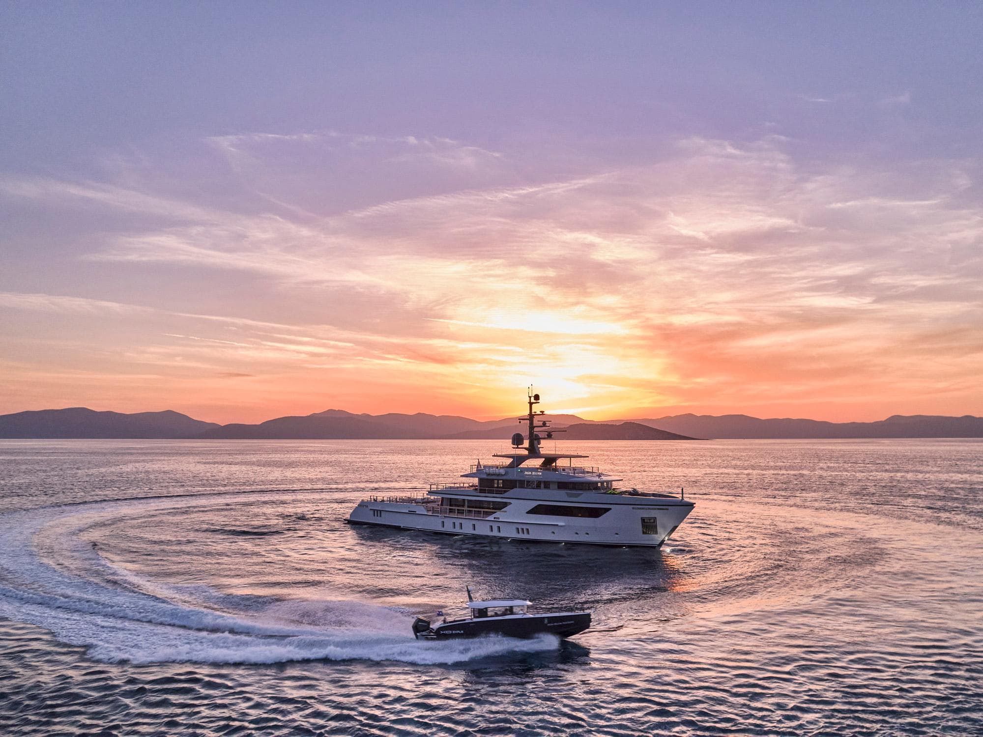 Sanlorenzo 500EXP yacht at sunset, 2023 model, with a speedboat in the foreground.