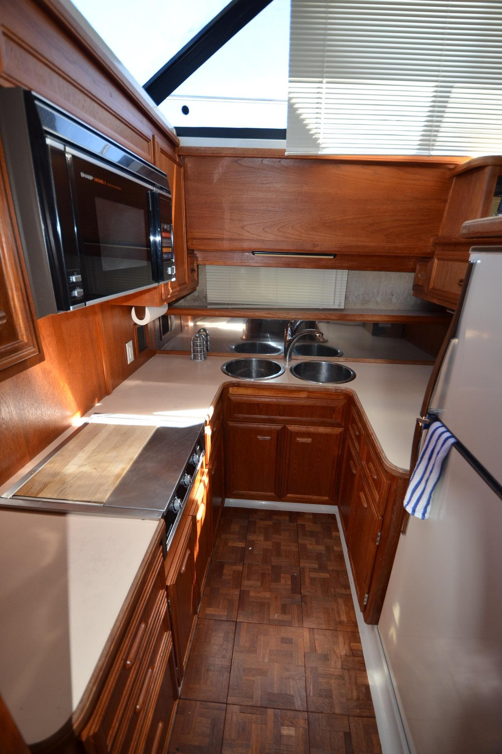 1987 Carver 4207 yacht kitchen with wood cabinetry, dual sinks, microwave, and refrigerator.