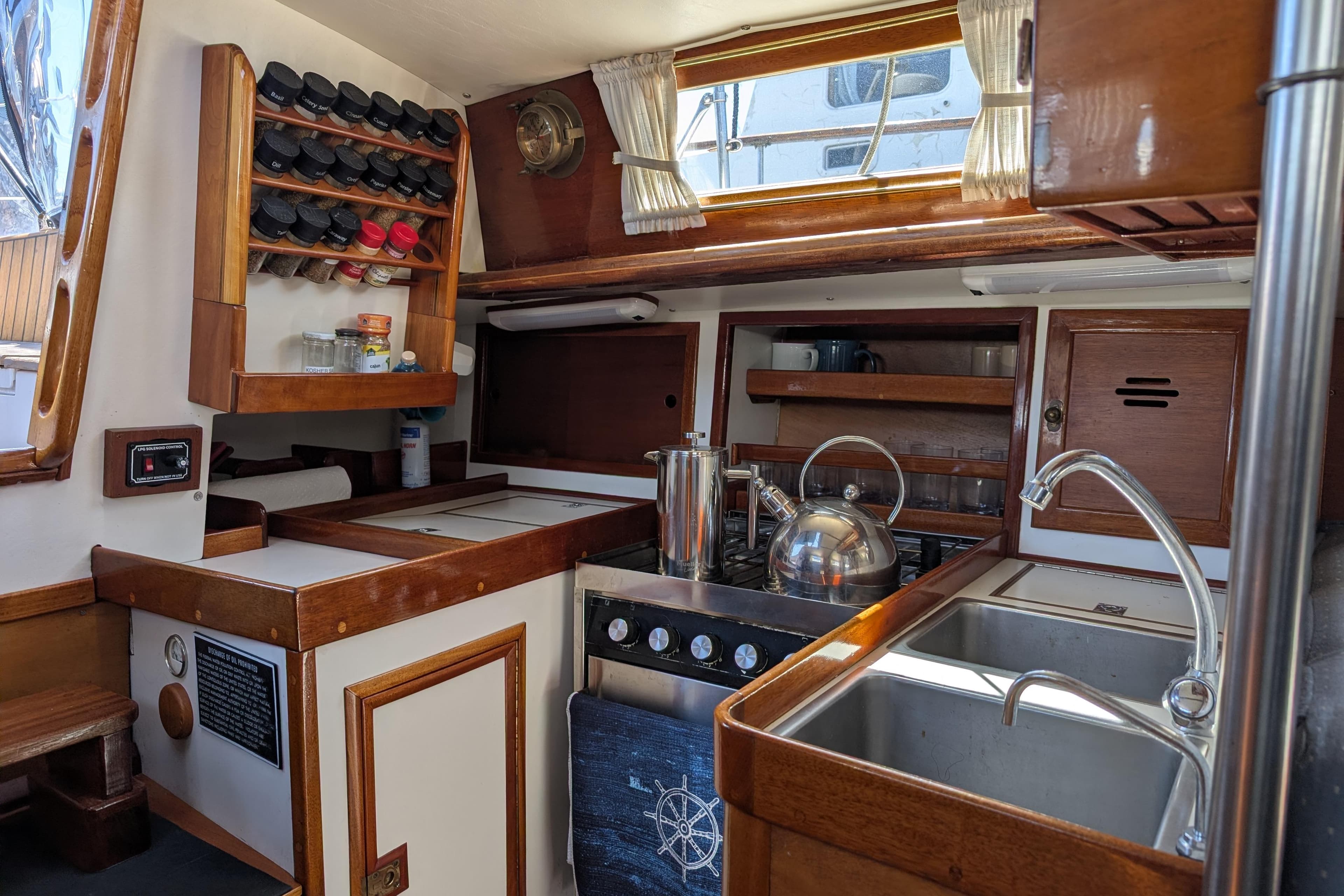 1984 Ohlson 38 yacht kitchen with wooden cabinetry, spice rack, and stainless steel sink.
