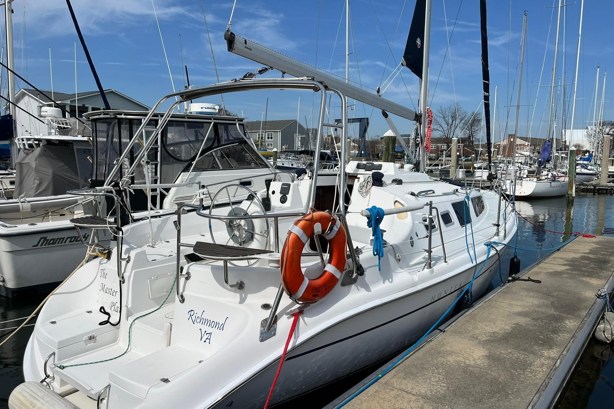 2002 Hunter 326 sailboat docked at marina, featuring lifebuoy and clear blue sky.