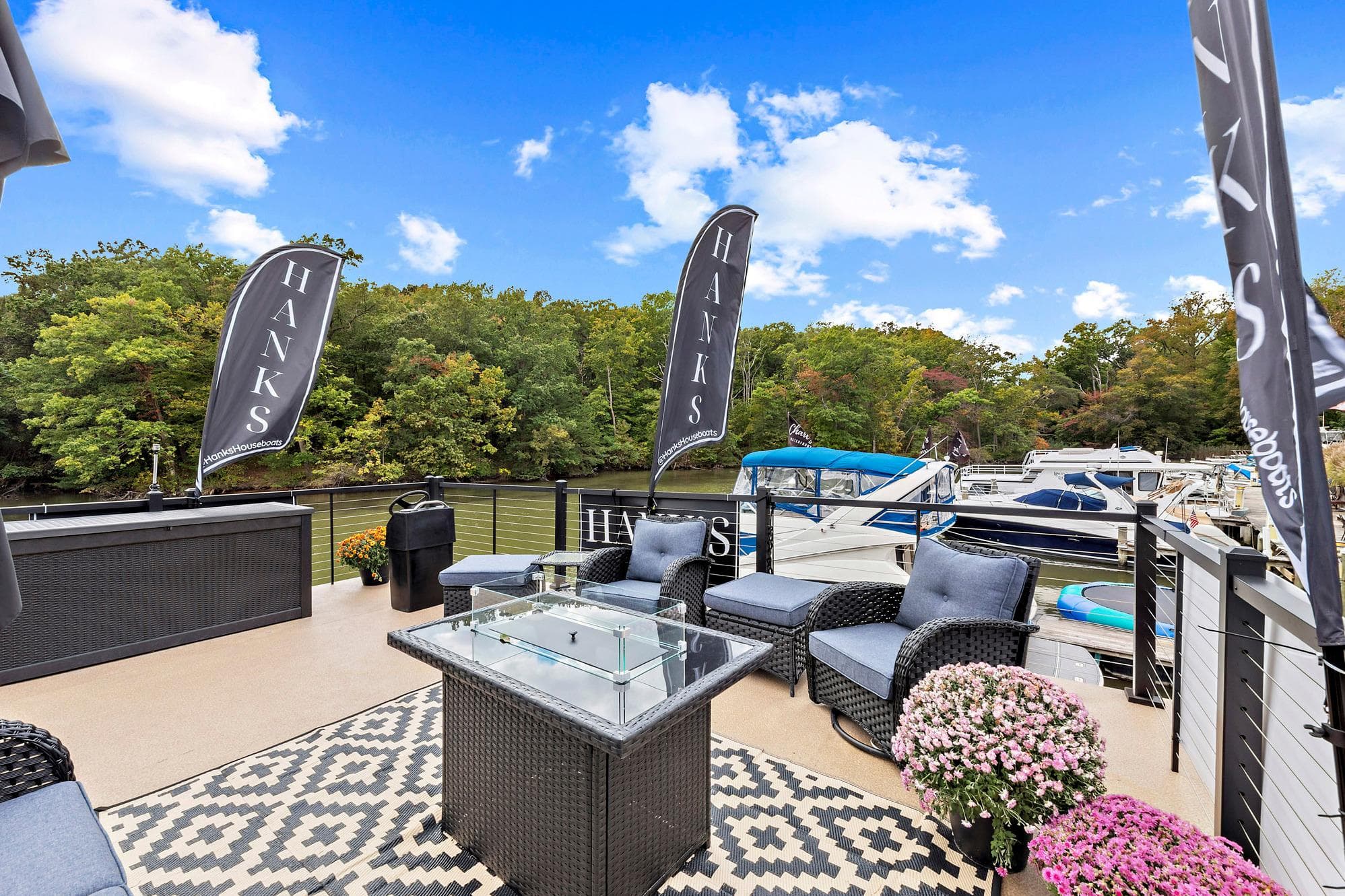 Luxurious 2026 Hanks 26 Houseboat deck with seating, flags, and scenic waterfront view.
