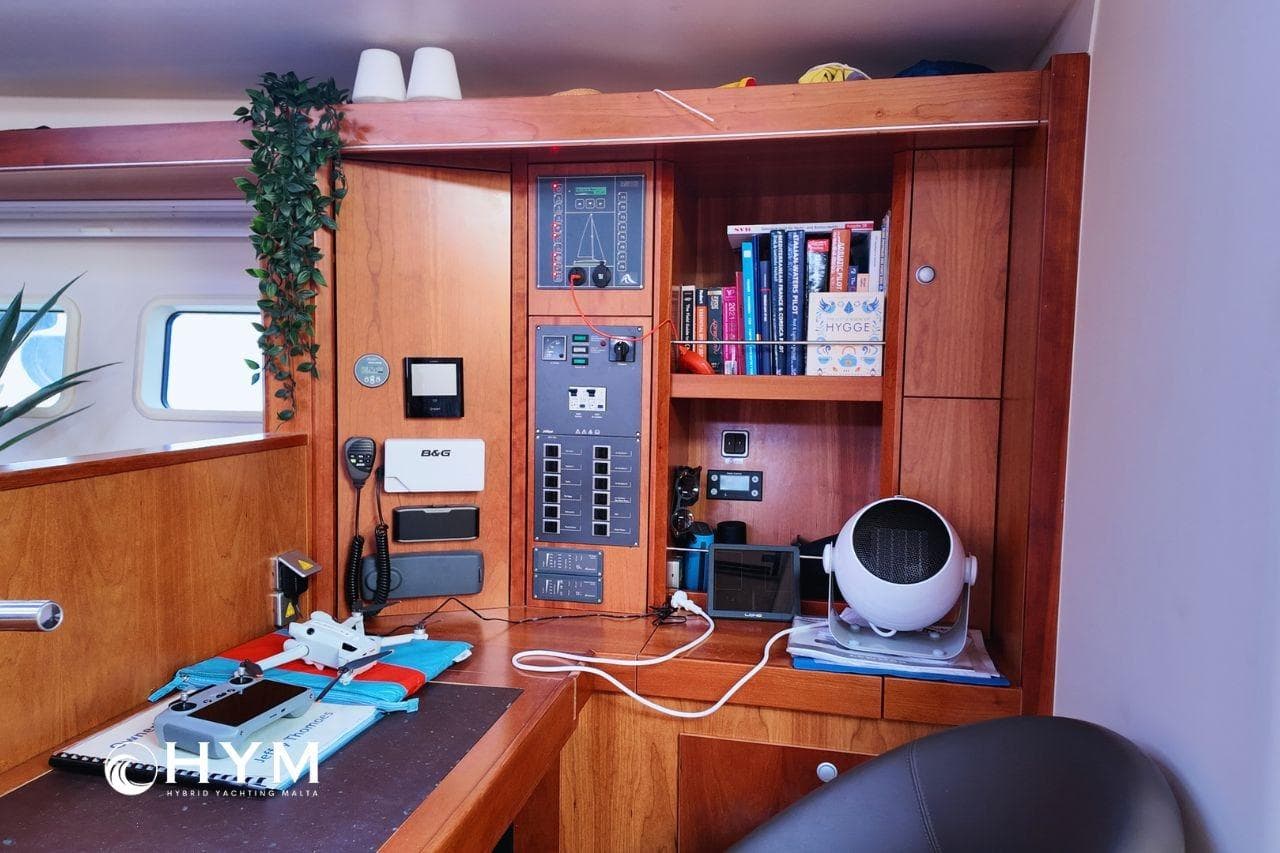 Interior of 2014 Hanse 575 yacht with navigation equipment and books on wooden shelves.