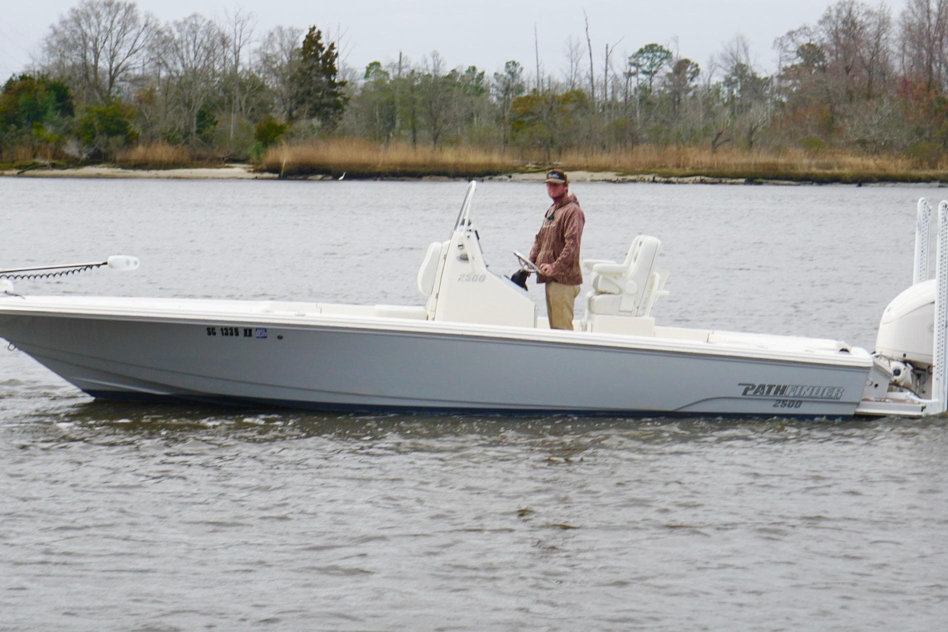 2023 Pathfinder 2500 Hybrid boat on a calm river with a person at the helm.