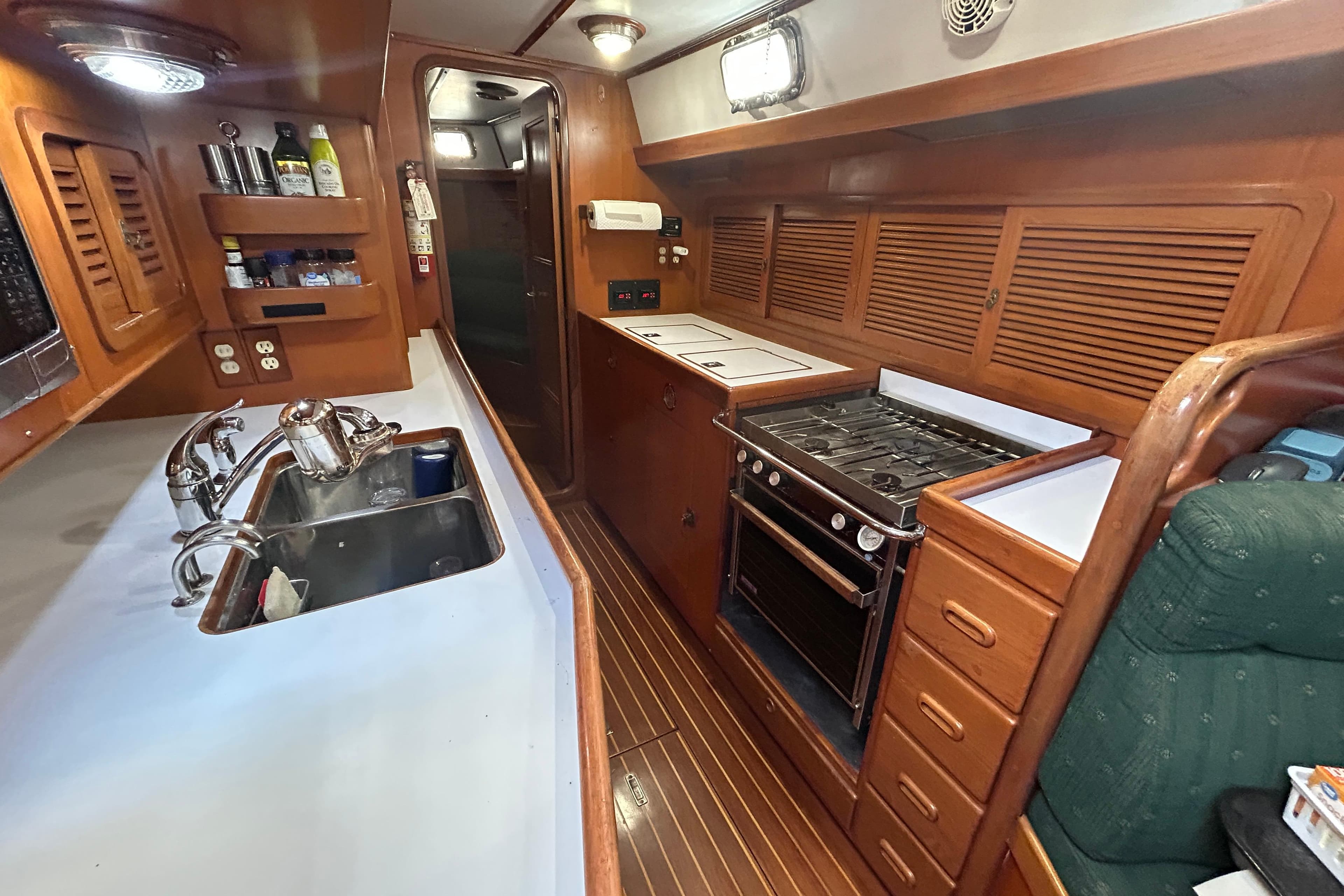 Interior of 1995 Tayana 48 yacht kitchen with stove, sink, and wooden cabinetry.