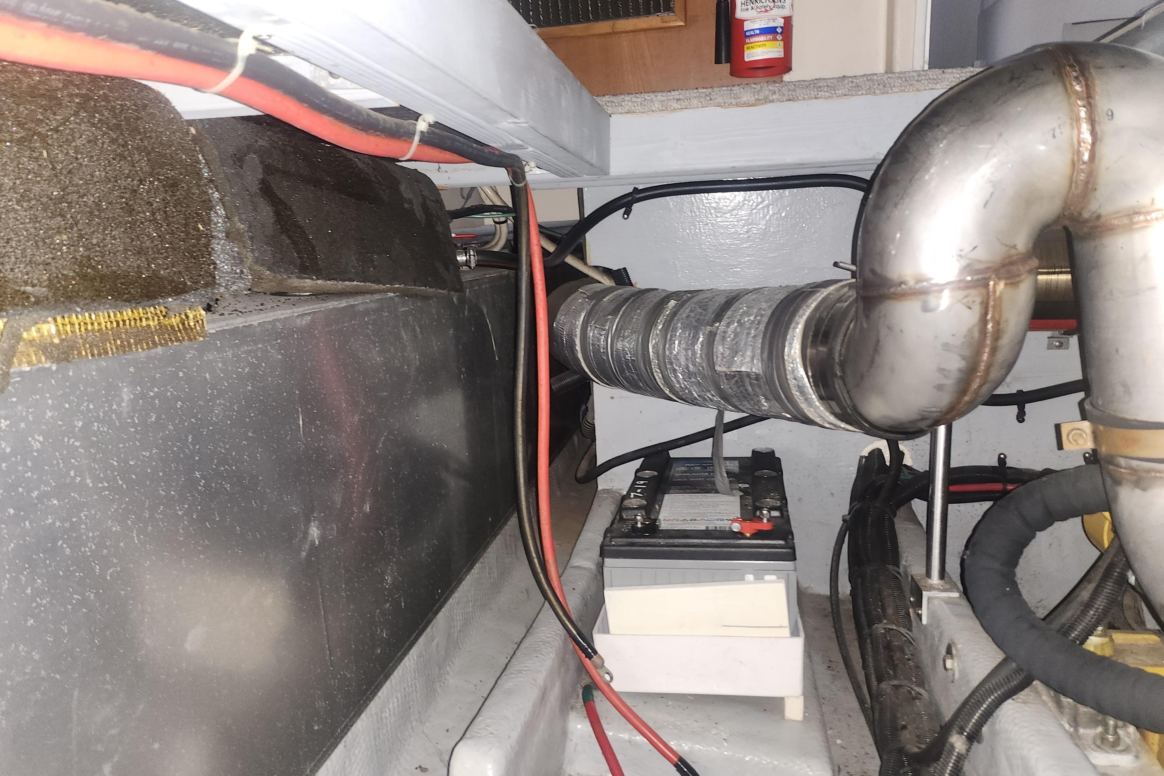 Engine room of a 1997 Mainship 350 Trawler with visible battery and exhaust system.