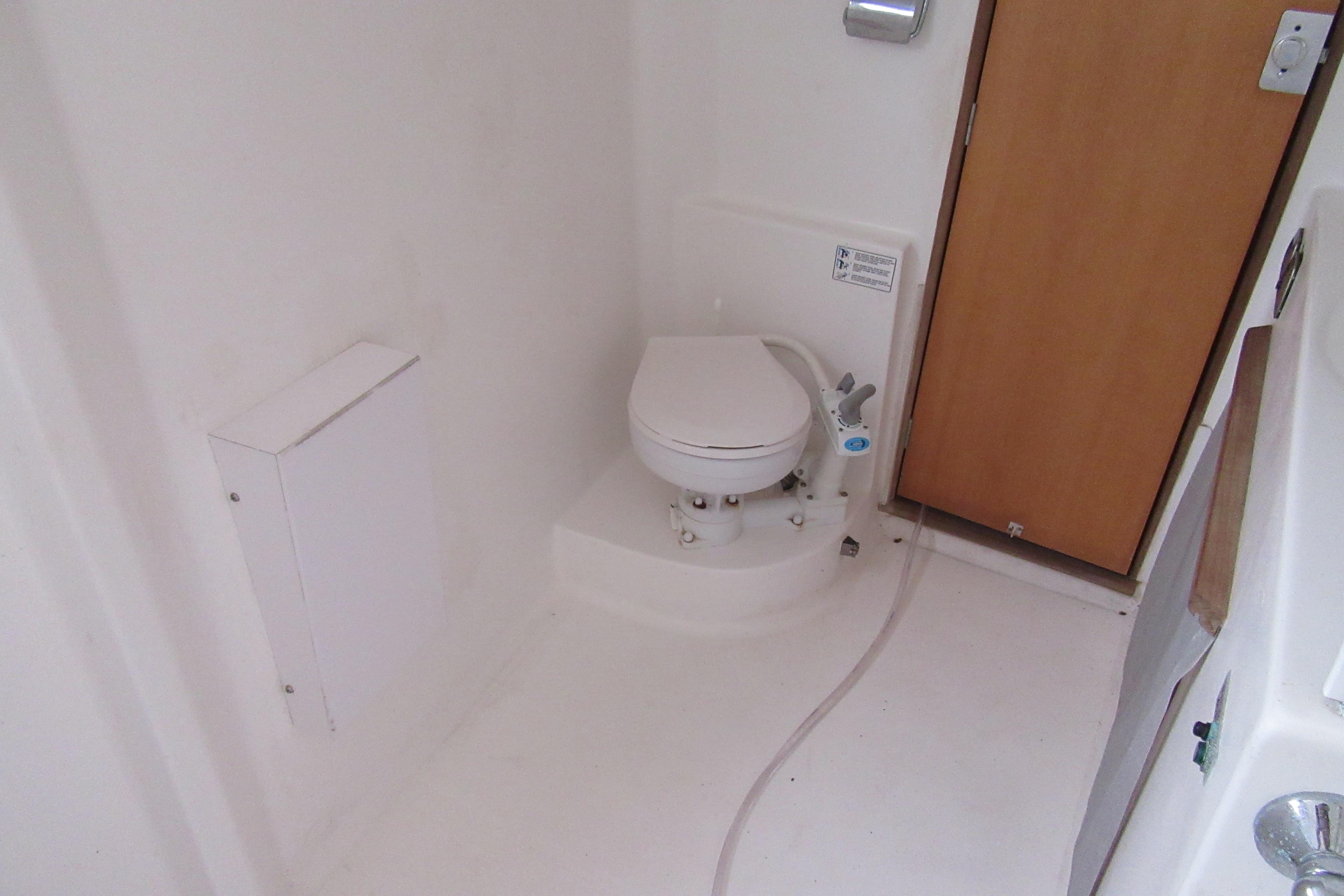 Compact marine bathroom in 2001 Catana 471 yacht, featuring a white toilet and wooden door.